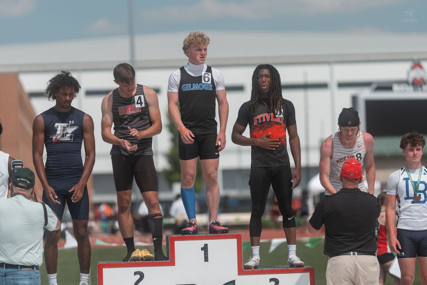 Teen boys receive medals on numbered award podium at outdoor OHSAA track and field championship.