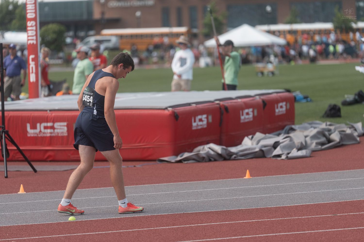 Female track athlete in navy and gold uniform walks along the red track at an outdoor athletic competition.