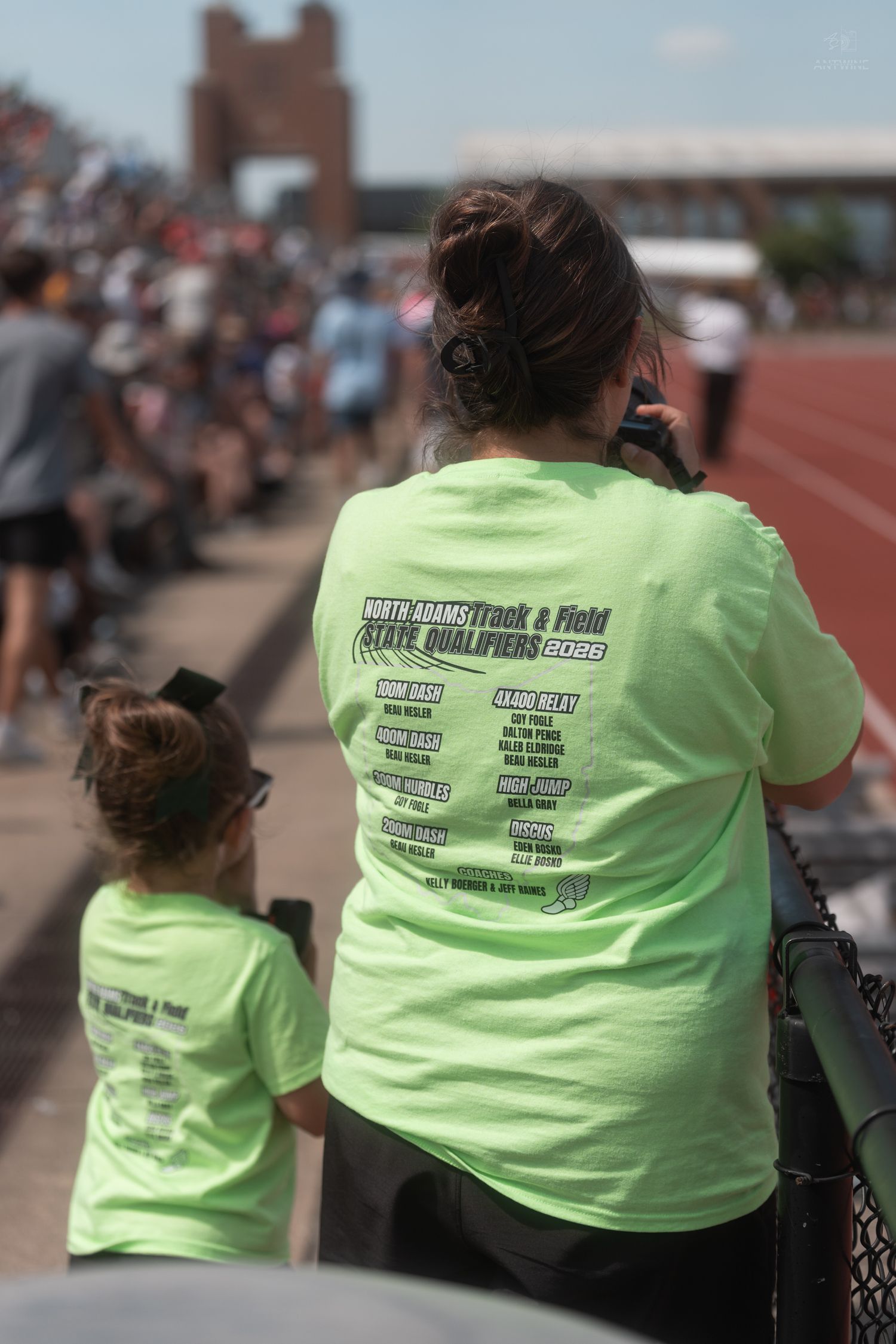 Woman and child wearing matching neon green North Adams Track and Field State Qualifiers shirts at a meet.