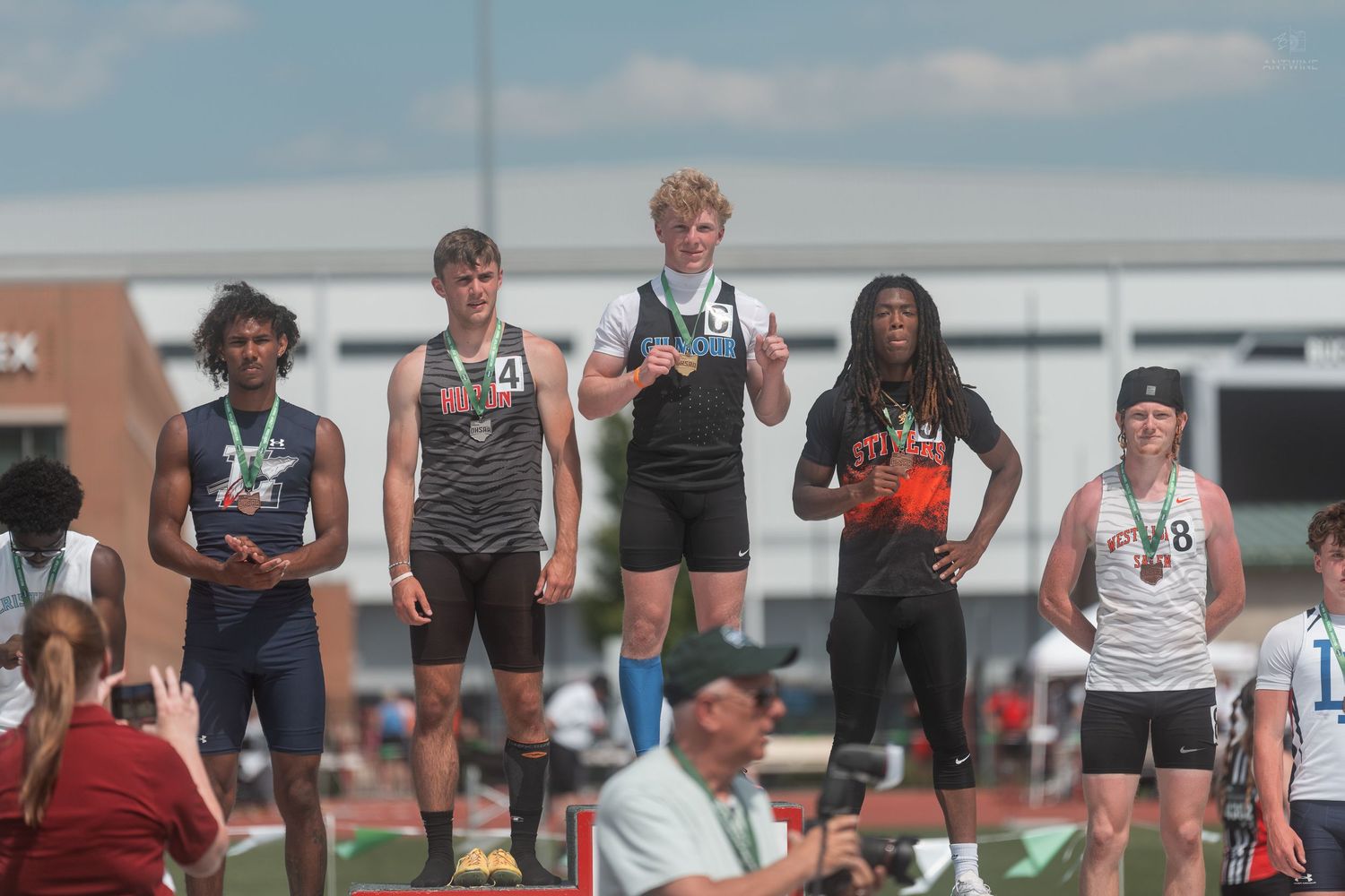 Five young male athletes stand on a tiered awards podium at an OHSAA high school track championship.