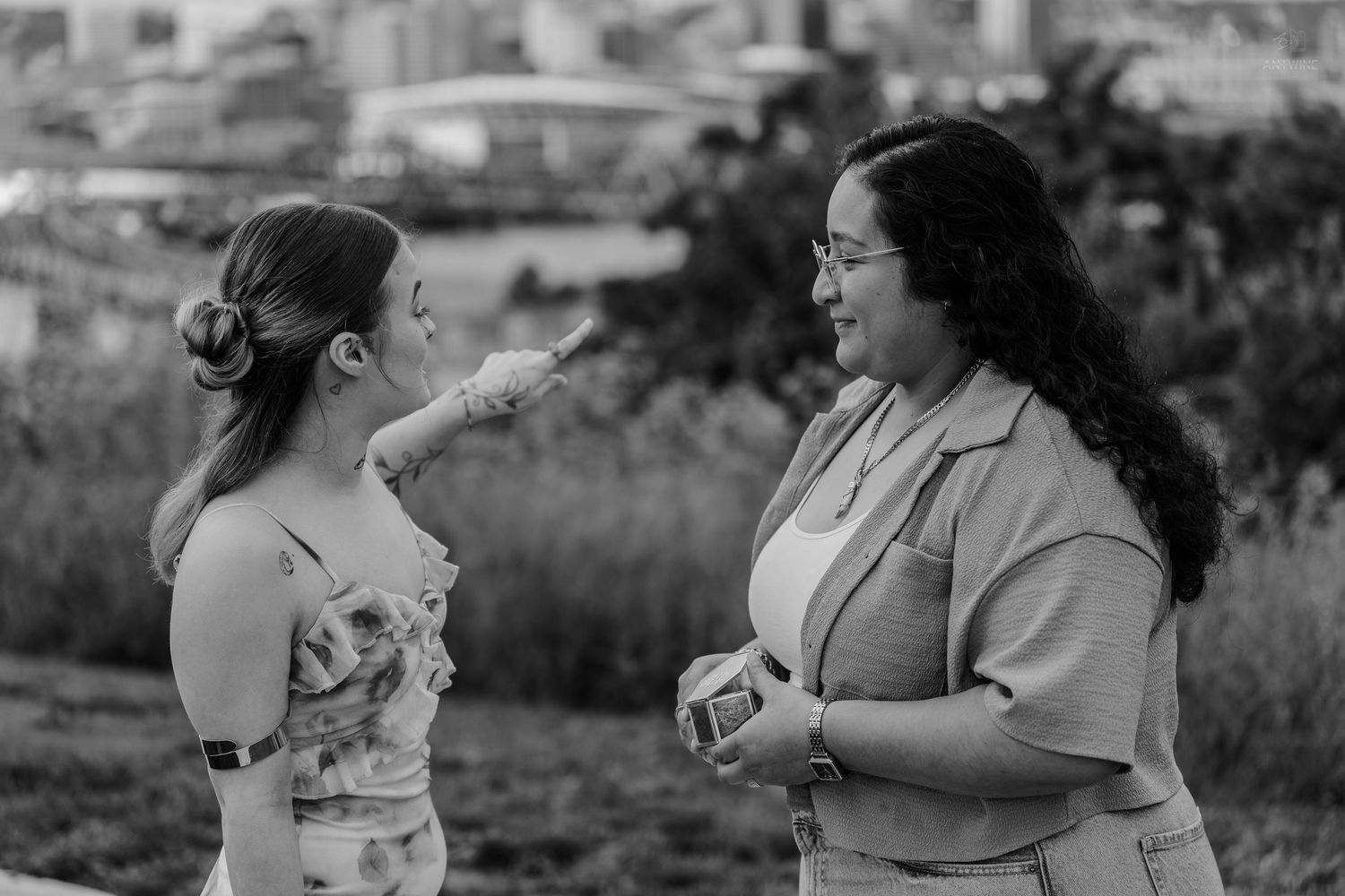 Black and white image of two women engaged in conversation on a green hilltop.