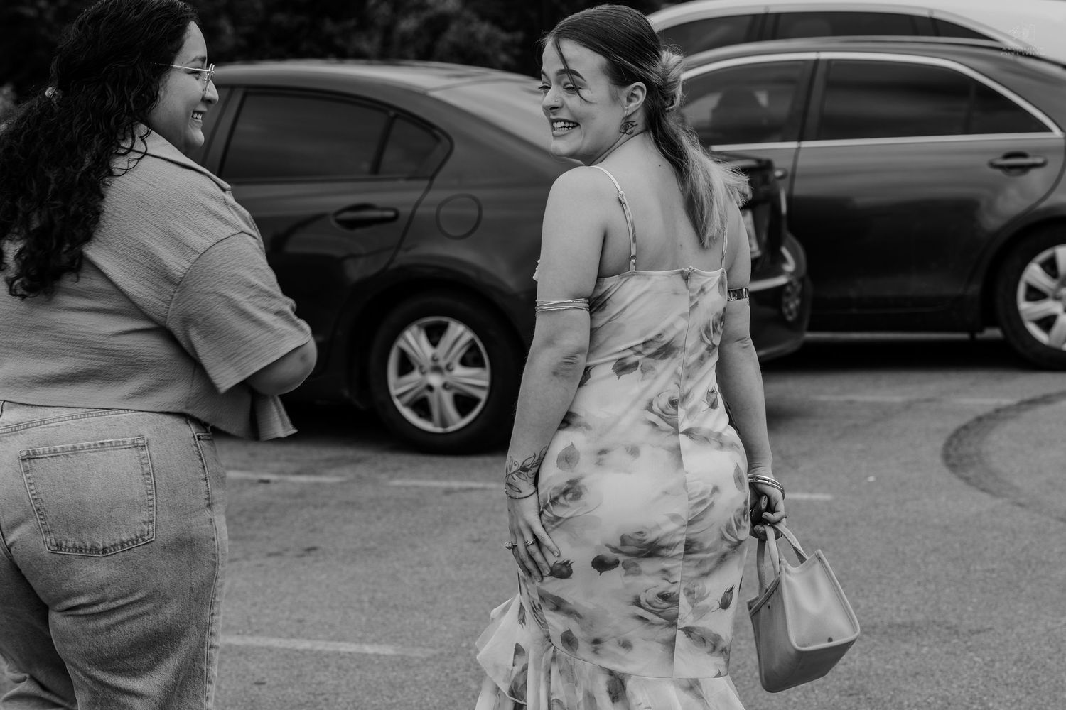 Two women share a joyful laugh together in a parking lot in this black and white candid shot.
