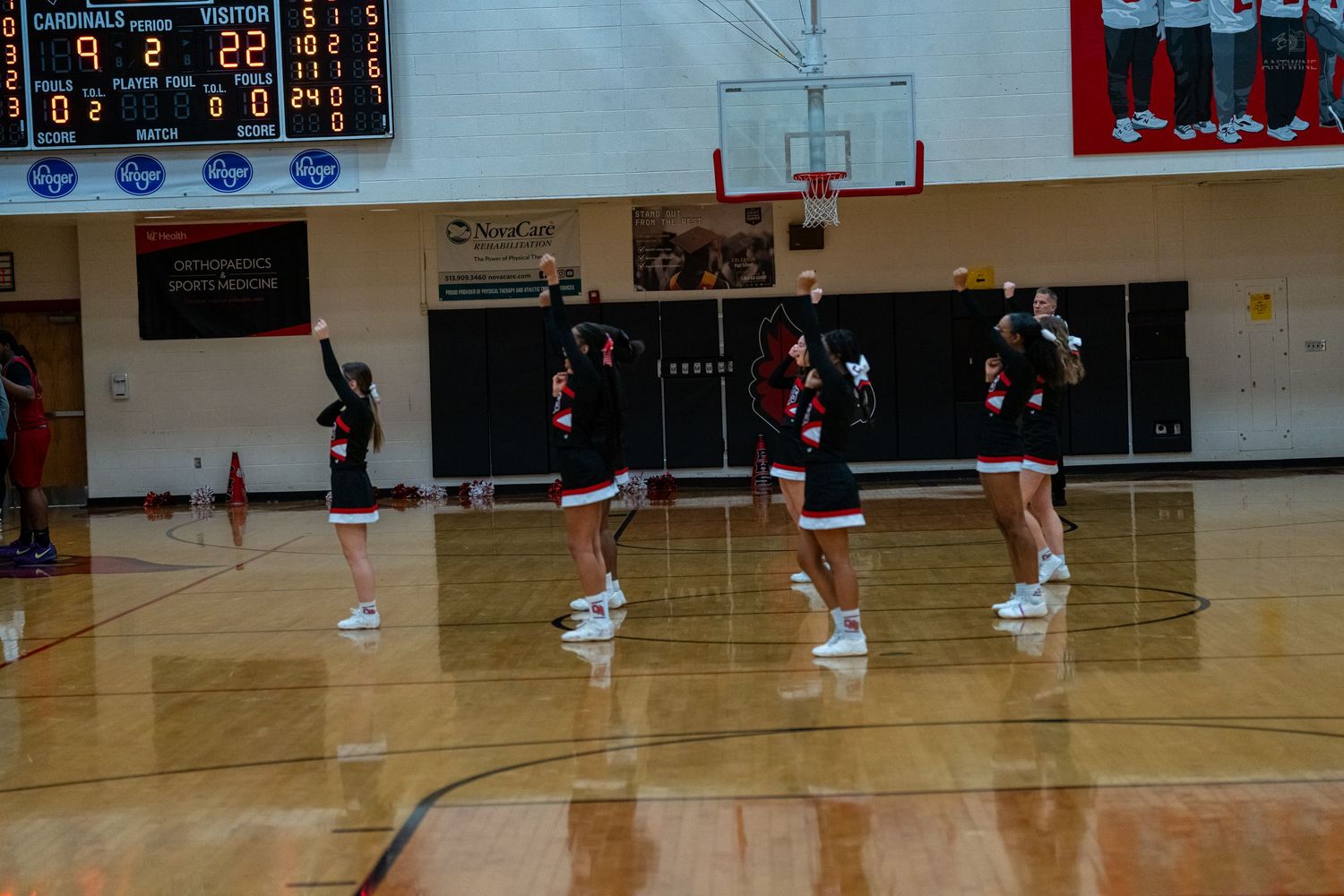 High school cheerleaders in black and red uniforms perform a sideline cheer during a basketball game.