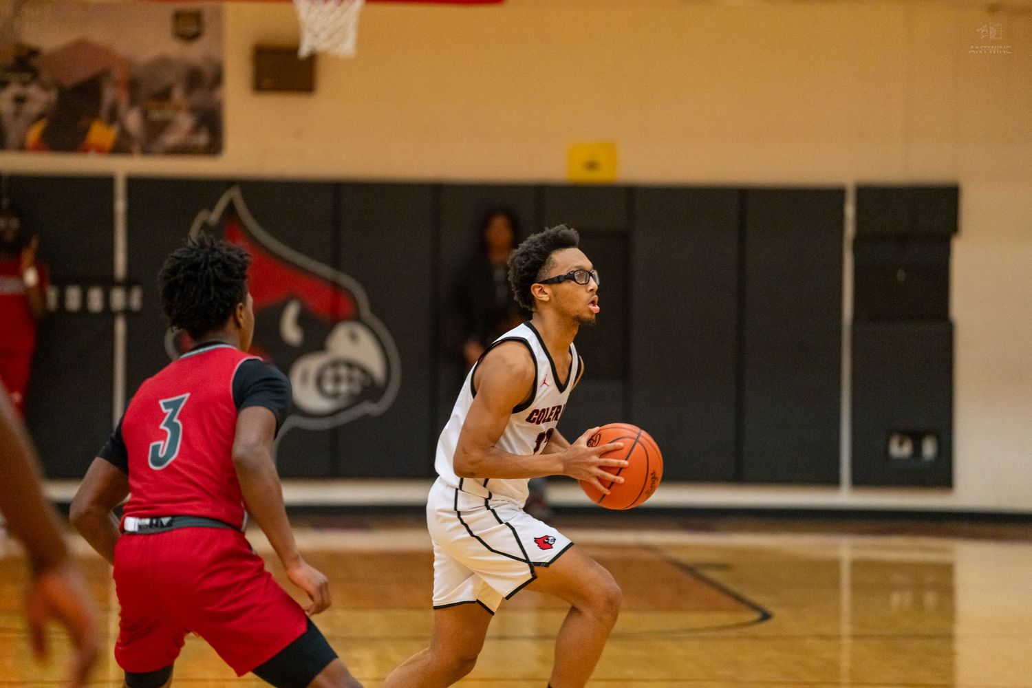 High school basketball player in white uniform prepares to shoot while defender in red jersey number 3 defends.