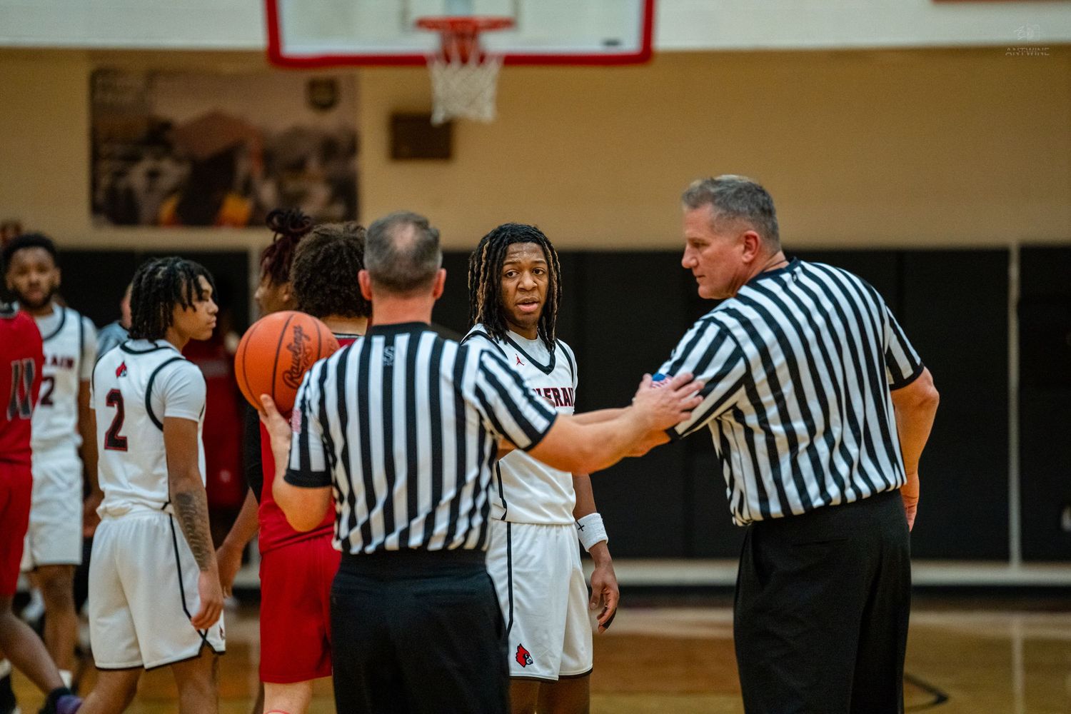 High school basketball player smiles while speaking with two referees during a timeout on the court.