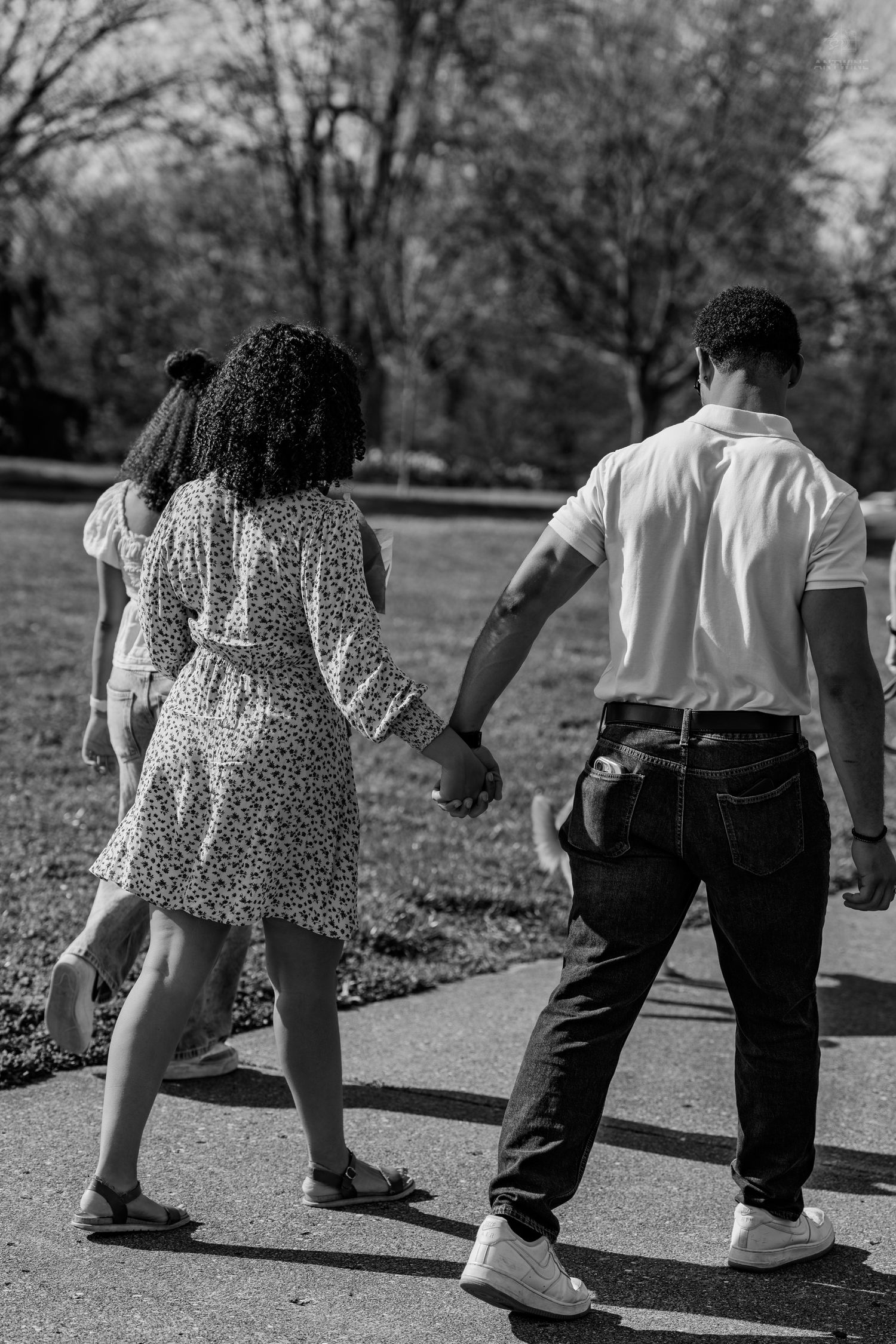 A couple holds hands while walking along a park path in black and white photography.