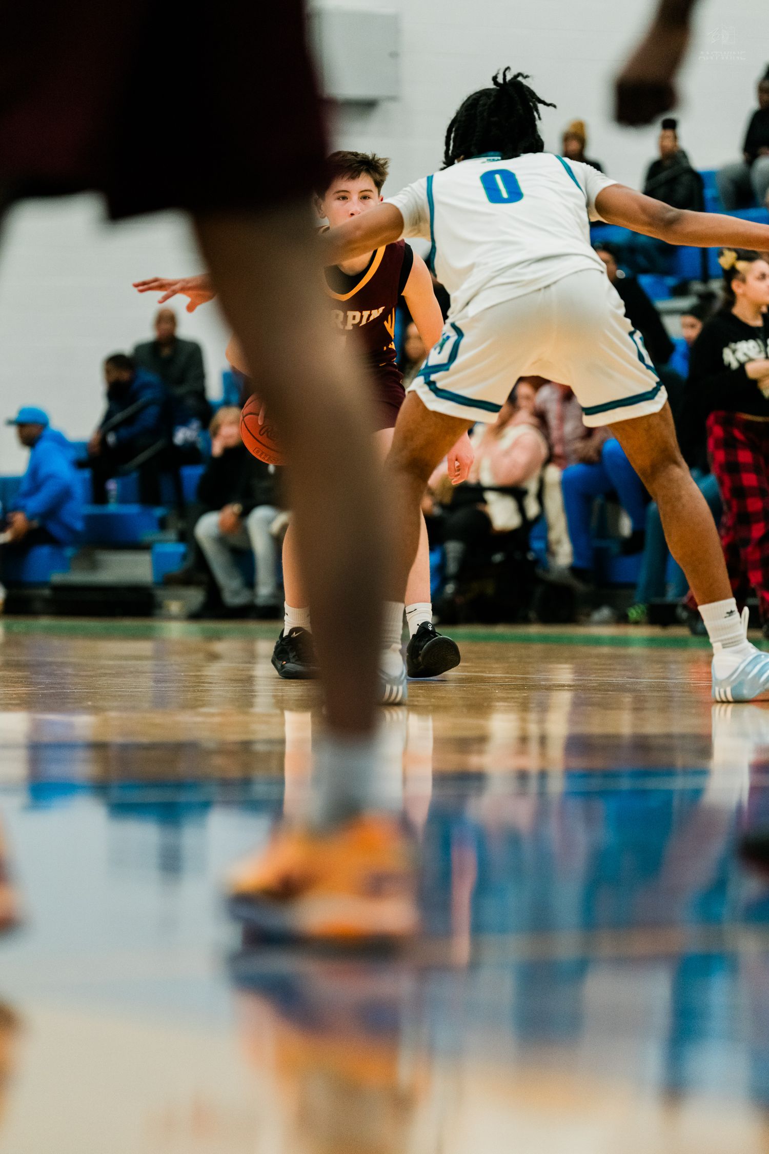 A basketball player in a white Warriors jersey dribbles against a defender in an orange uniform during a high school game.