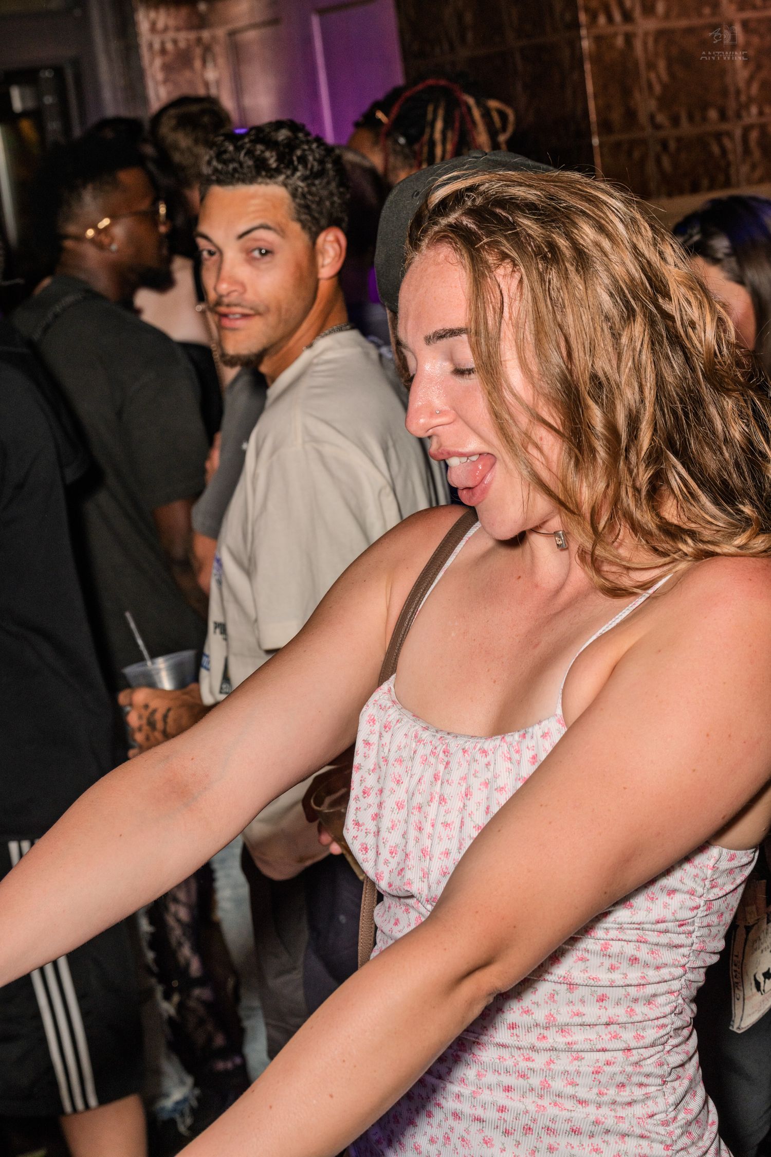 Energetic young woman in floral dress dancing enthusiastically at a nightclub event.