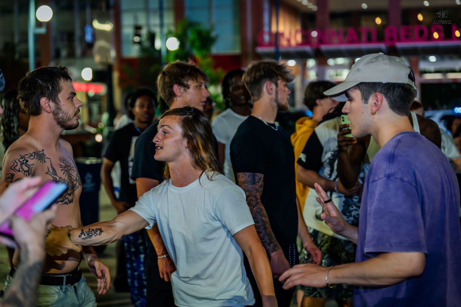 Young people socializing on urban street at night with city lights behind.
