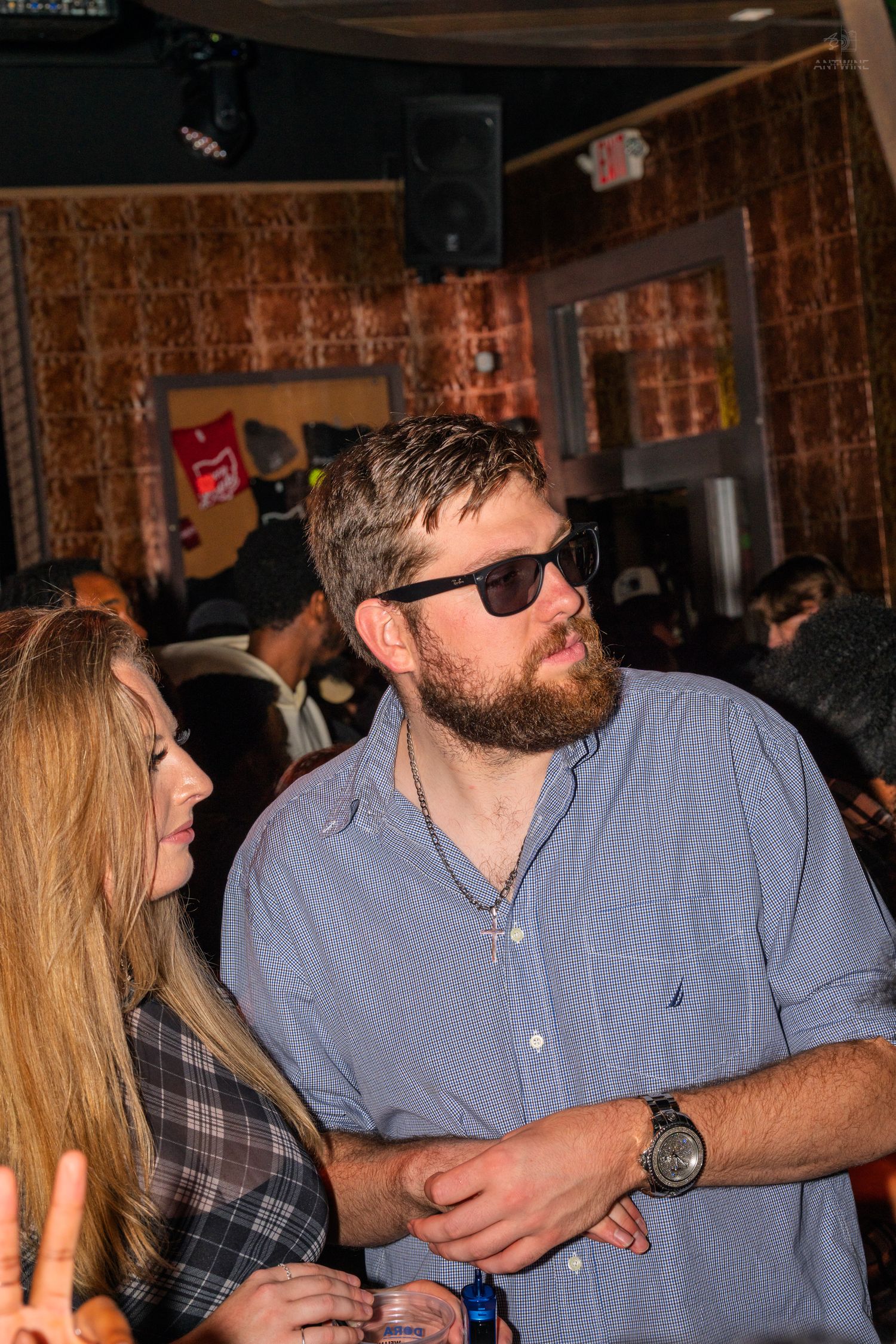 Bearded man in sunglasses and blue shirt standing with woman at a nightclub.