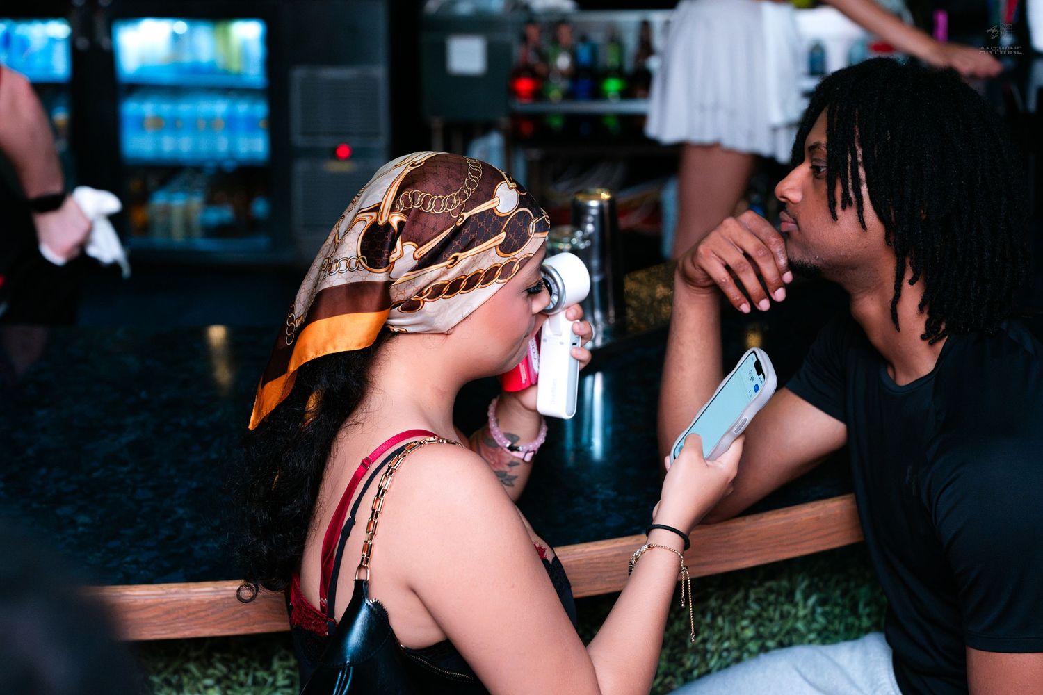 Couple sharing an intimate moment at a bar, woman wearing decorative headscarf holding a drink.