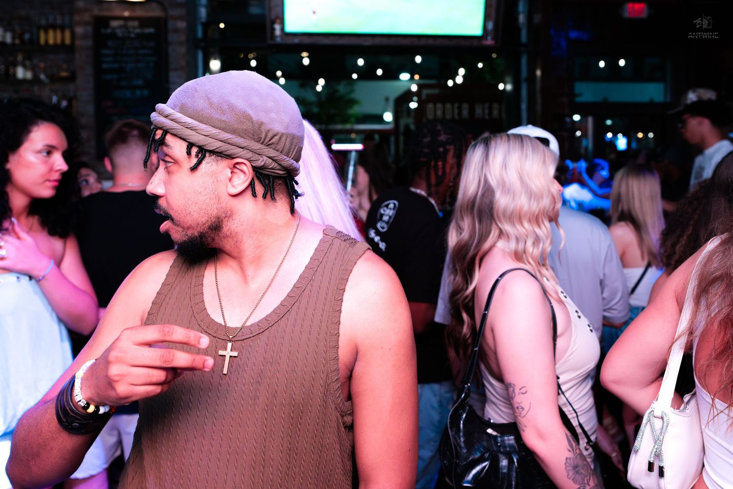 Man wearing cross necklace and cap socializing at a nightclub.