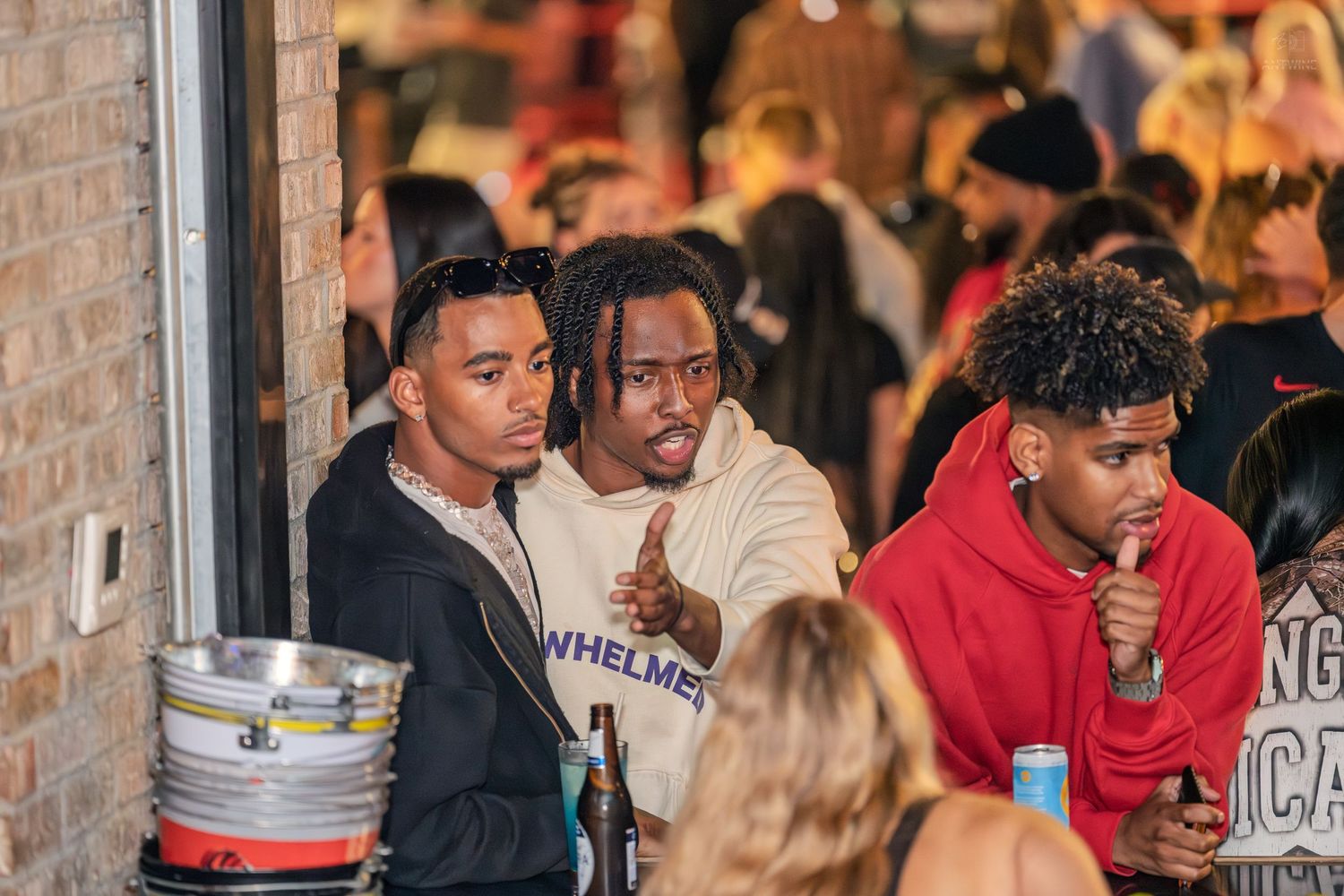 Three young men posing together at a crowded outdoor nightclub event at night.