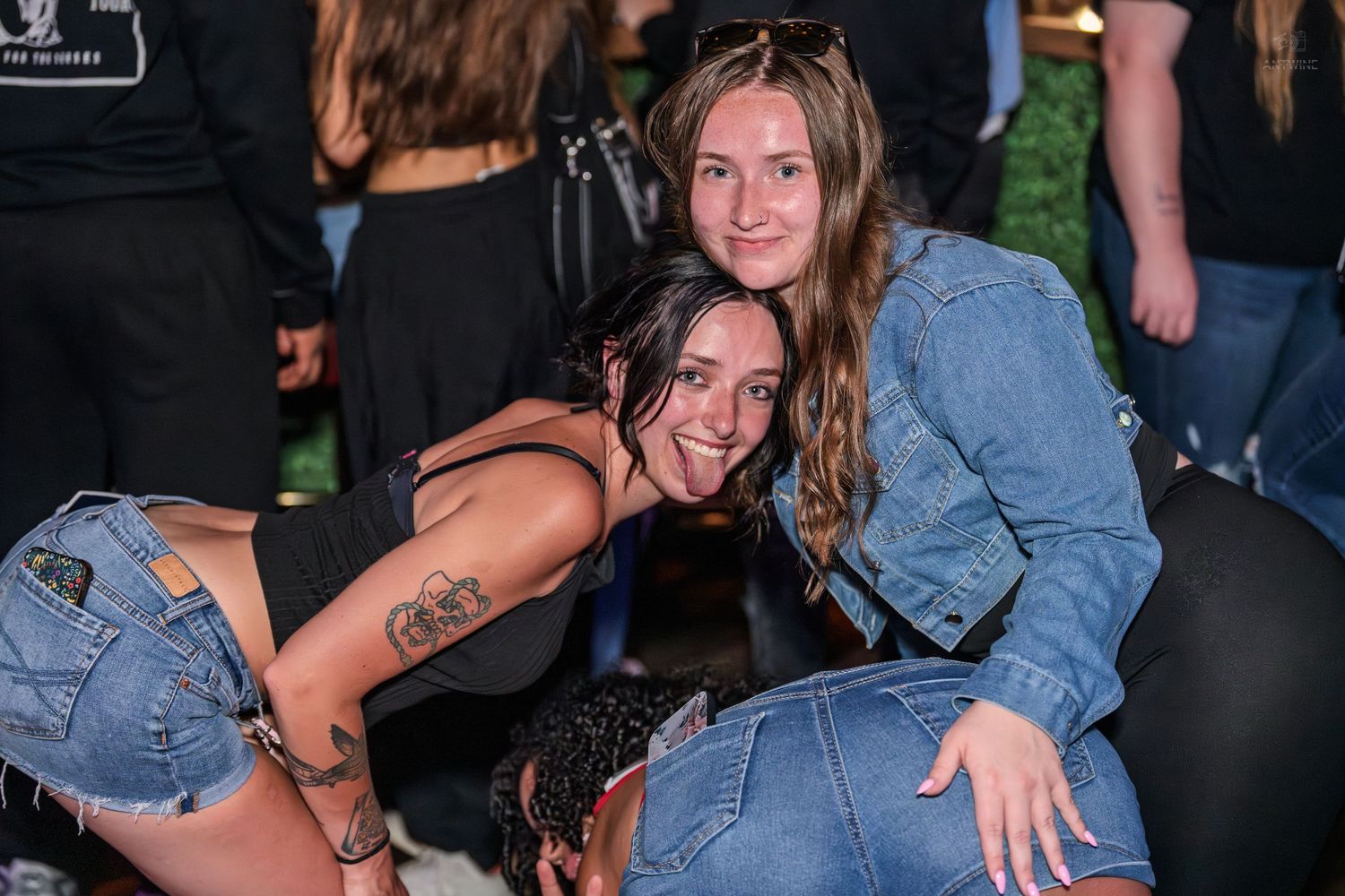Two smiling young women crouching together for a photo at an outdoor evening party.
