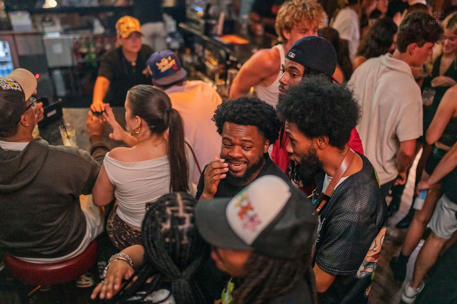 Group of smiling young men enjoying conversation and laughing together at a crowded nightclub gathering.