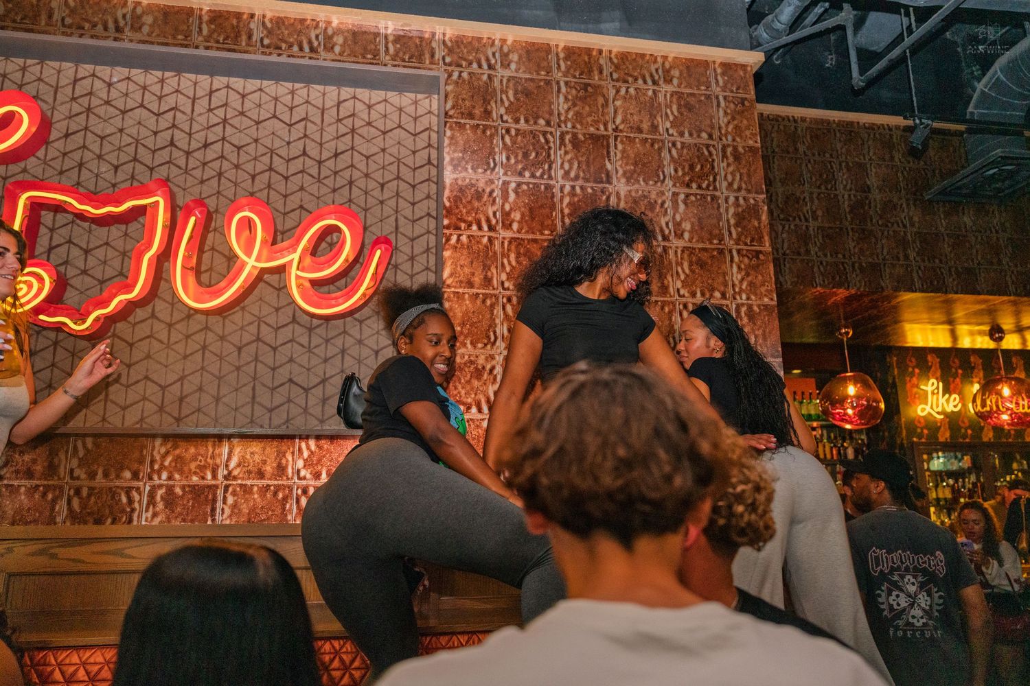 People dancing on elevated platform near Love neon sign at Cincinnati nightclub.
