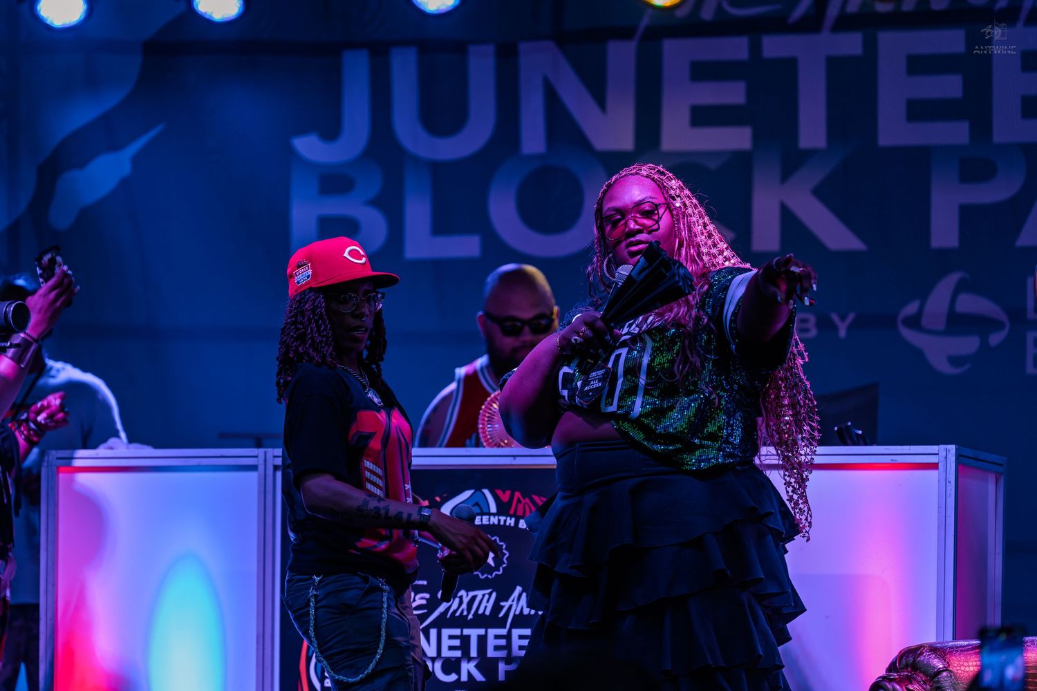 Female artist performing on stage at Juneteenth Block Party wearing green patterned outfit under blue lights.