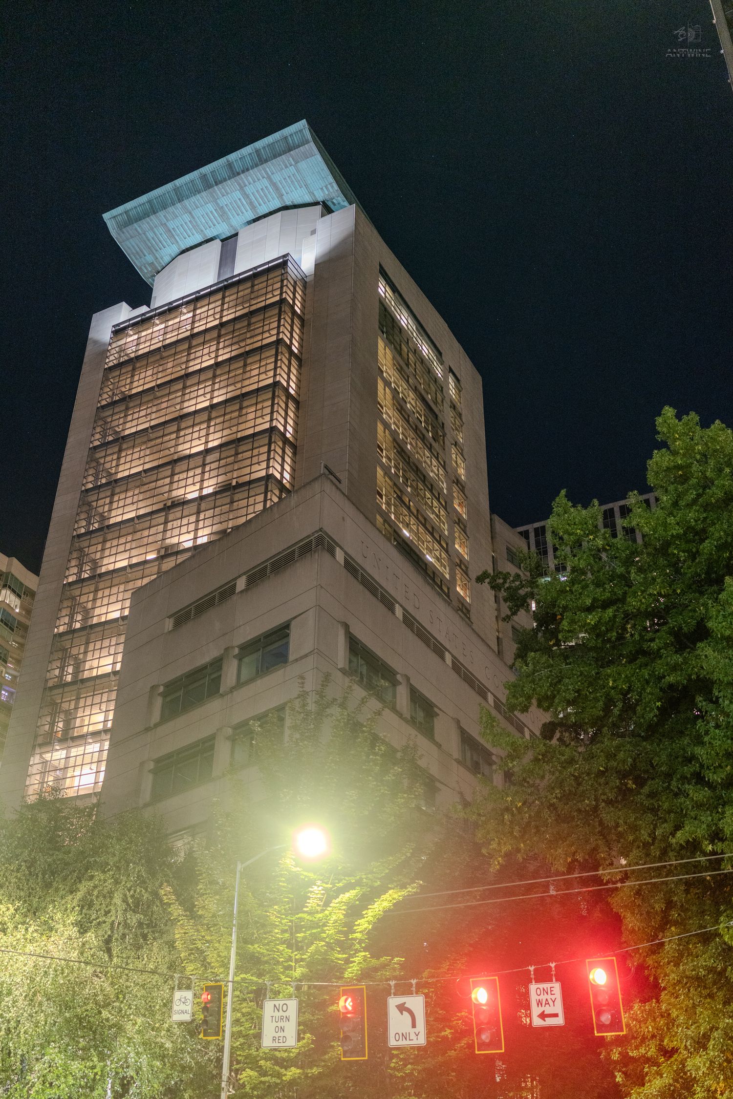 Tall office building illuminated at night with glowing windows and a lit street corner below.