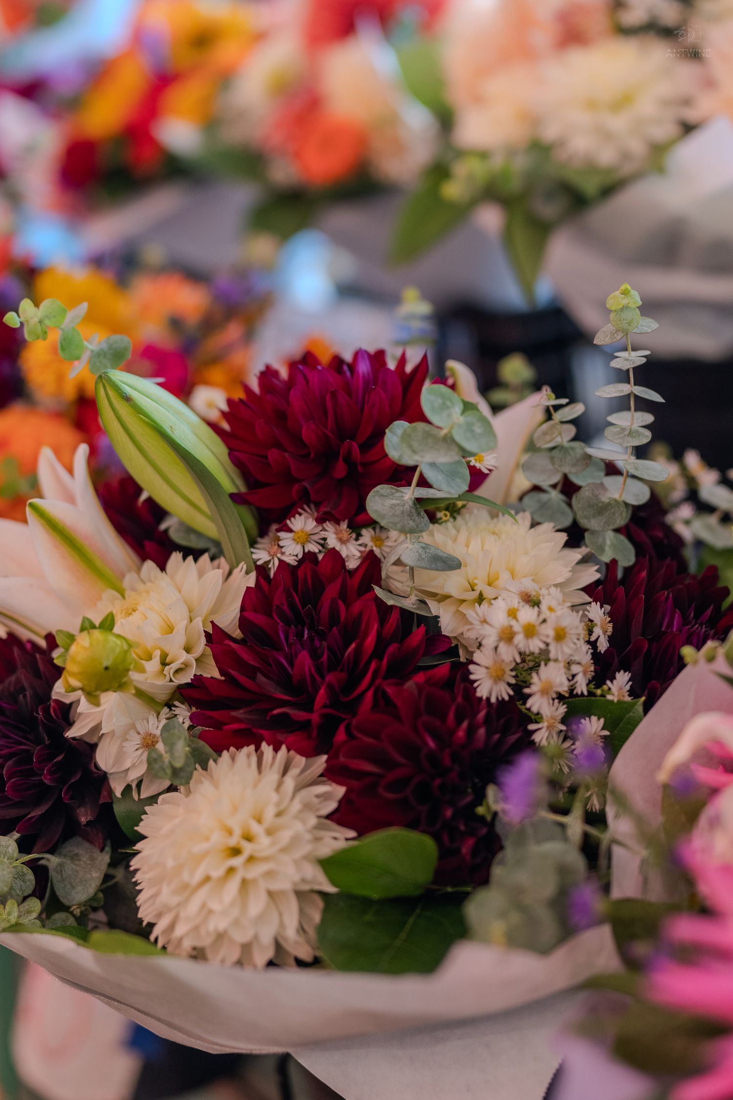 Vibrant bouquet of dark red dahlias, white chrysanthemums, and eucalyptus at a flower market.