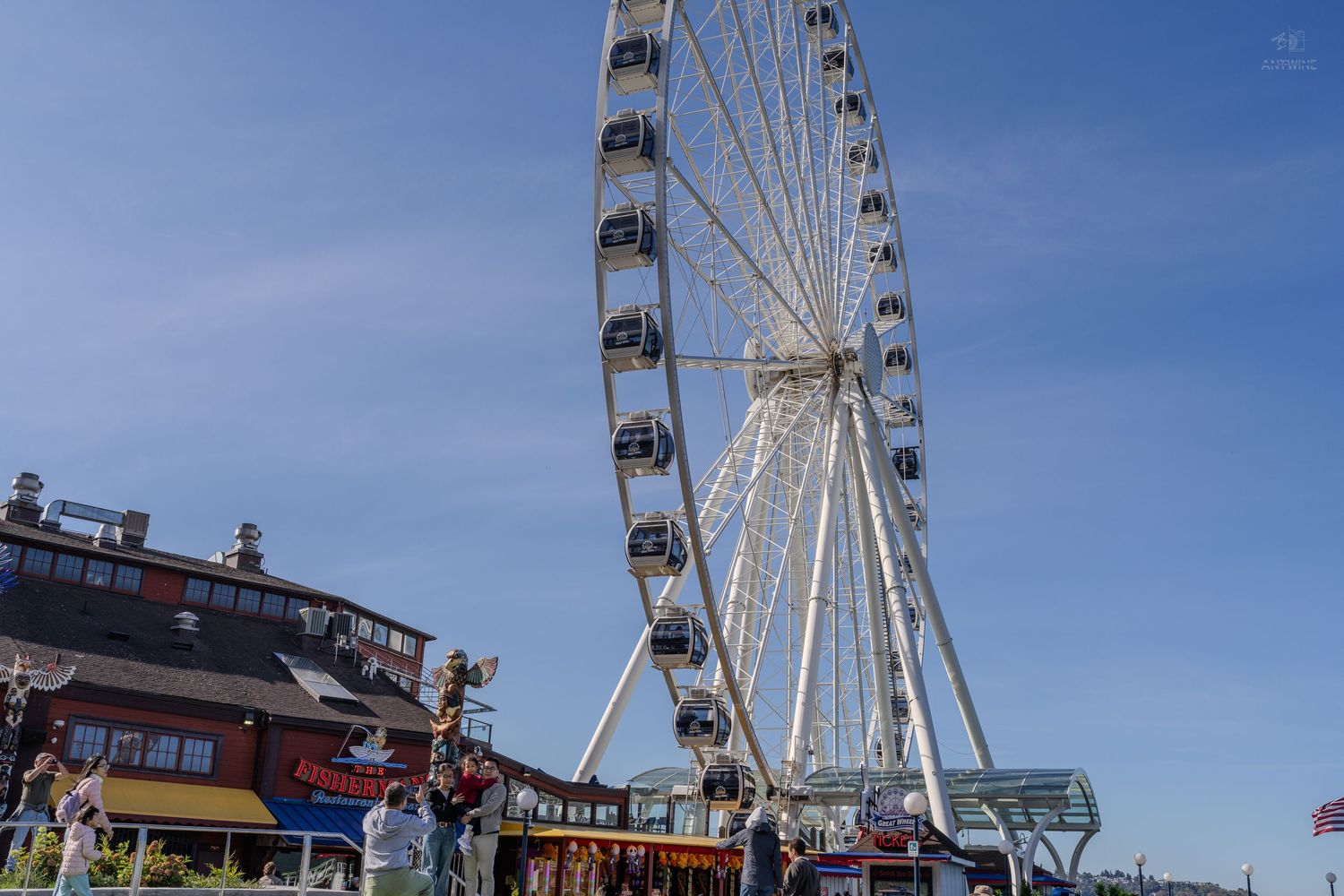The Seattle Great Wheel ferris wheel rises against a blue sky at Pier 57 on the Seattle waterfront.