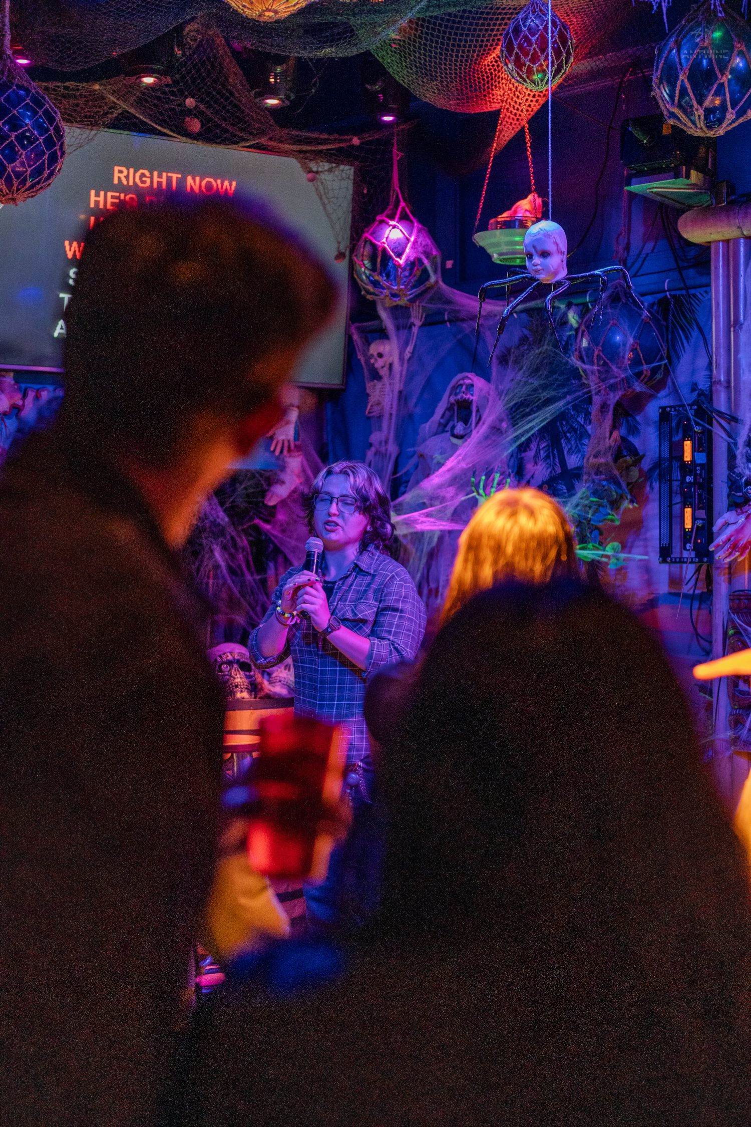 Person singing karaoke in a dimly lit bar with purple neon lights and Halloween decorations.