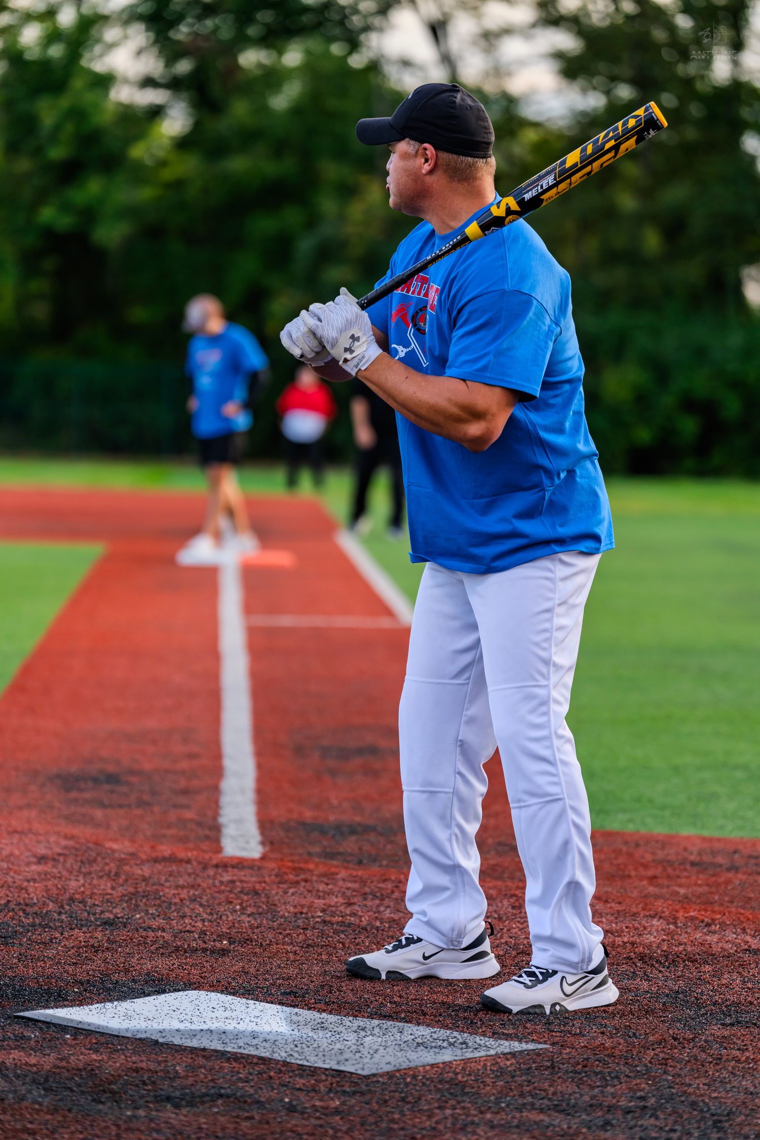 A baseball player in a blue jersey and white pants stands at home plate holding a bat over his shoulder.