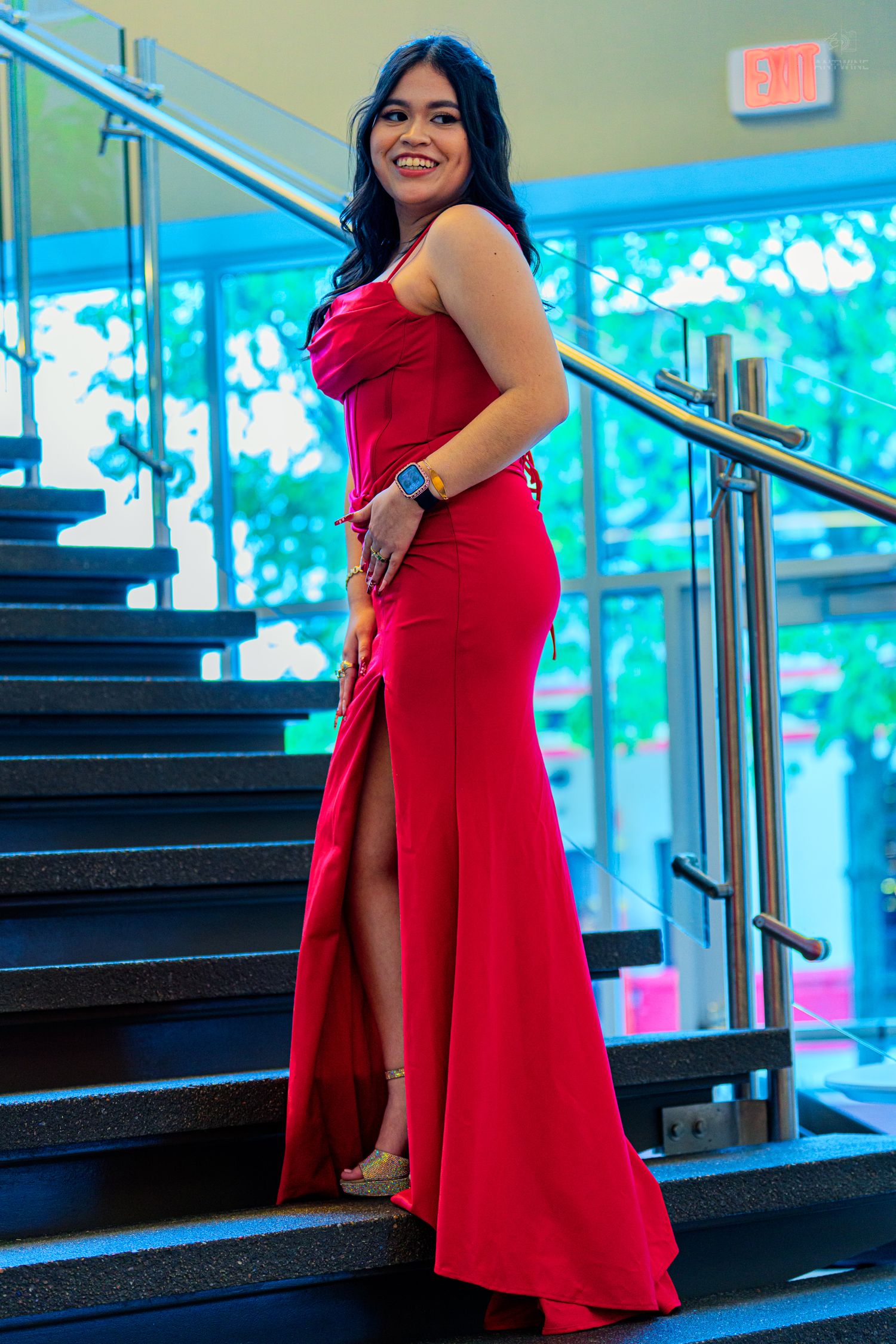 Young woman in elegant red slit gown posing on stairs at formal event.
