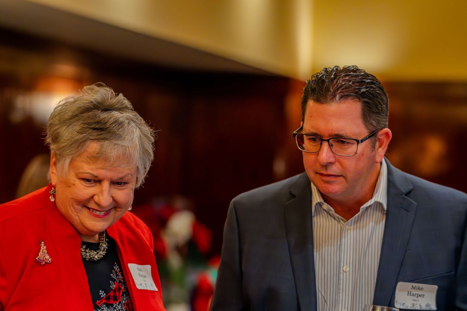 Two professionals in formal attire smiling and conversing at a networking event or holiday gathering.