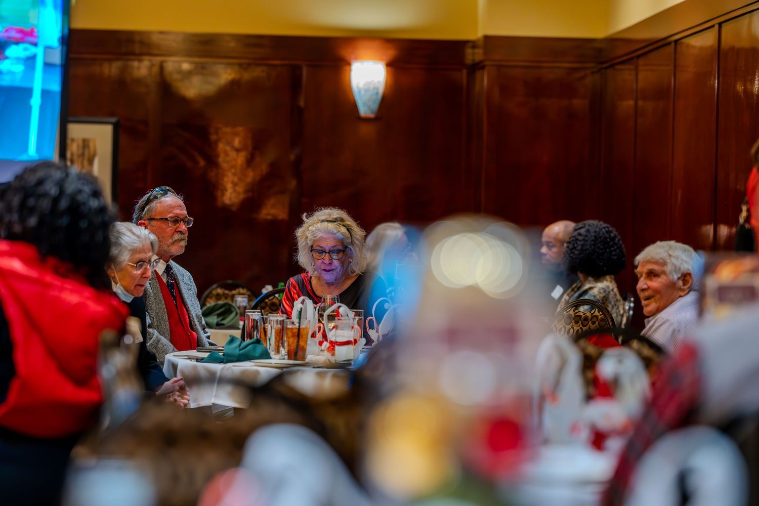 Elderly guests gathered around a festive dining table during a holiday party in an elegant wood-paneled restaurant.