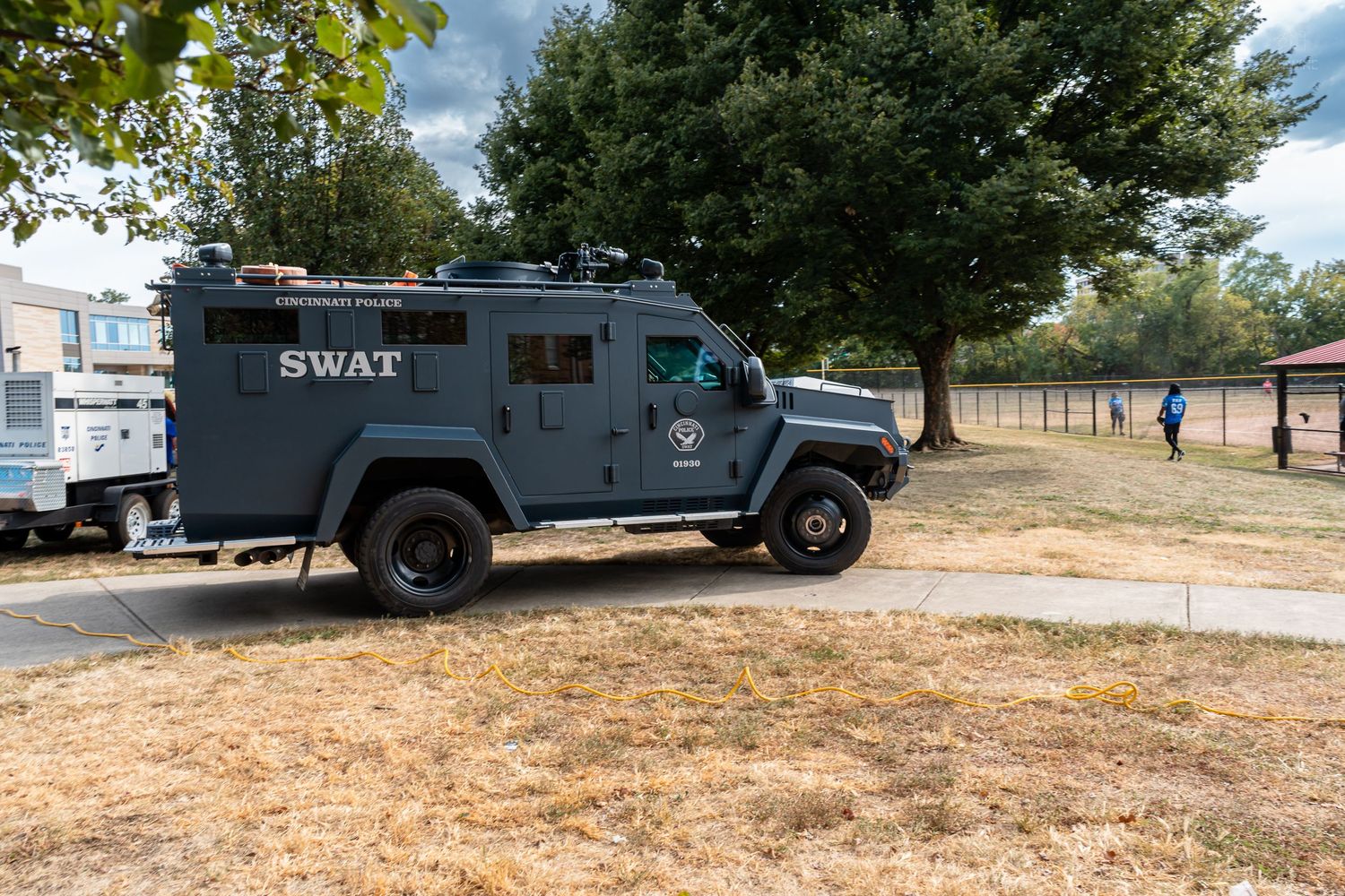 A gray SWAT armored tactical vehicle parked in a park area on a sunny day.