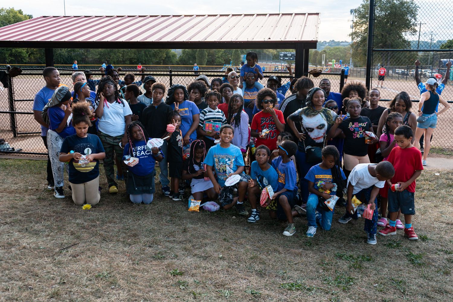 Diverse group of kids and adults gathered at a baseball field for a community youth sports program.