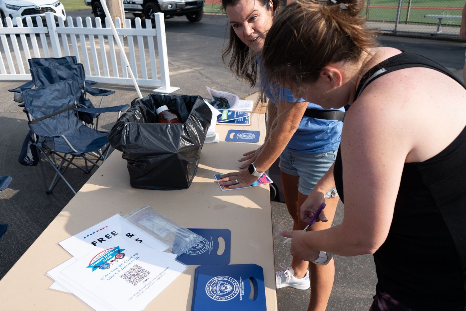 Two women signing up at an outdoor information table with brochures and branded materials at a community event.