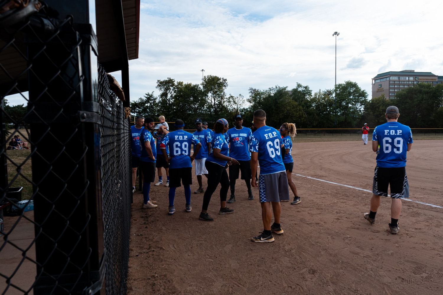 A team in blue number 69 softball jerseys huddles together on a dirt field during a recreational game.