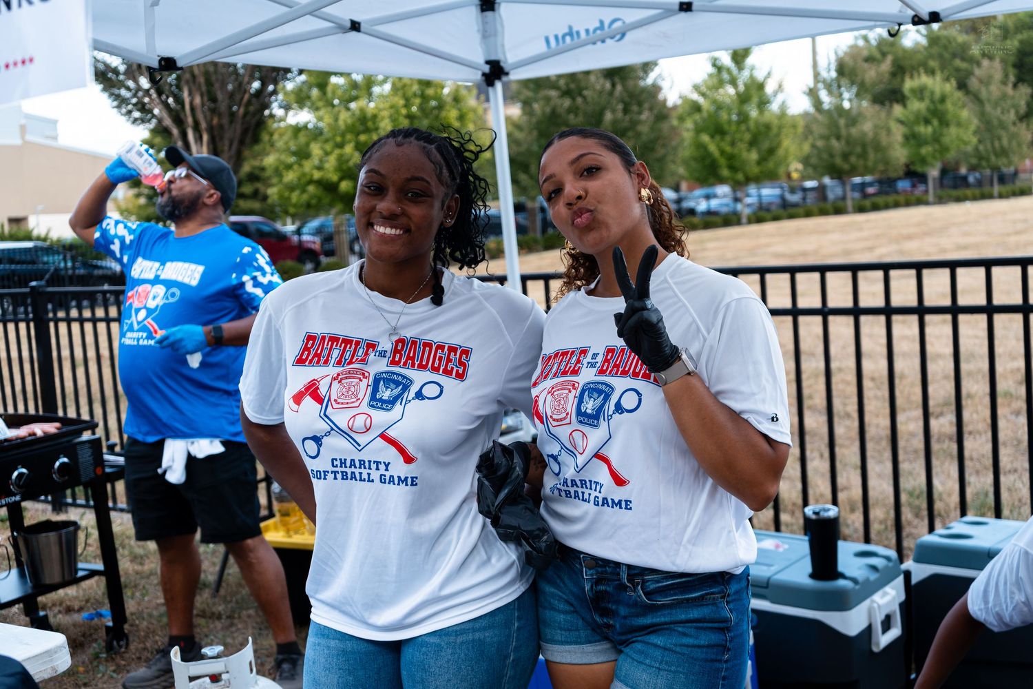 Two women pose in matching Battle of the Badges charity softball game t-shirts at an outdoor event.