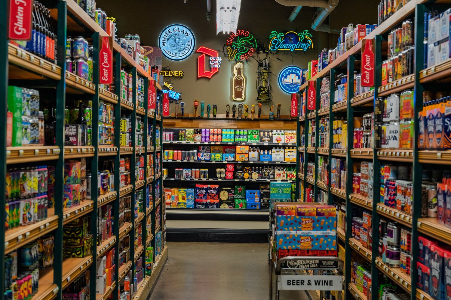 Colorful beer and wine store aisle with neon signs and shelves stocked with various craft beer cans and bottles.
