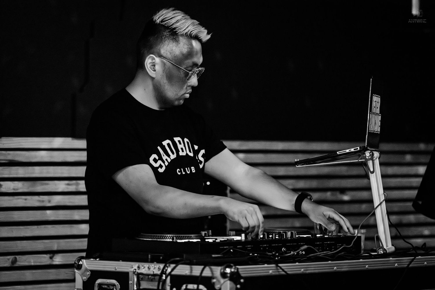 DJ mixing music on turntables outdoors, wearing a black t-shirt and glasses in a black and white photo.