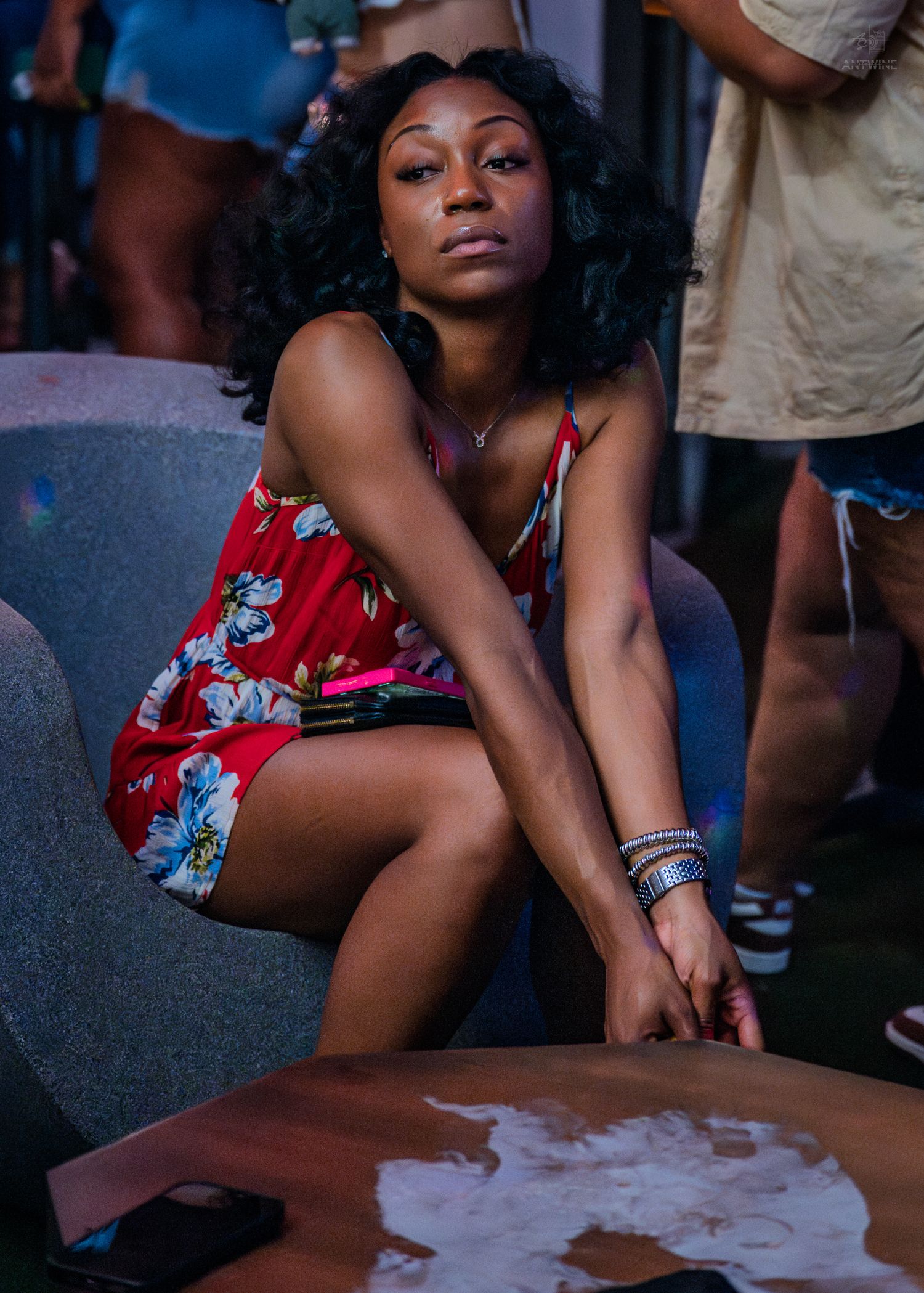 A young woman in a red floral dress sits at a table during an outdoor party event.