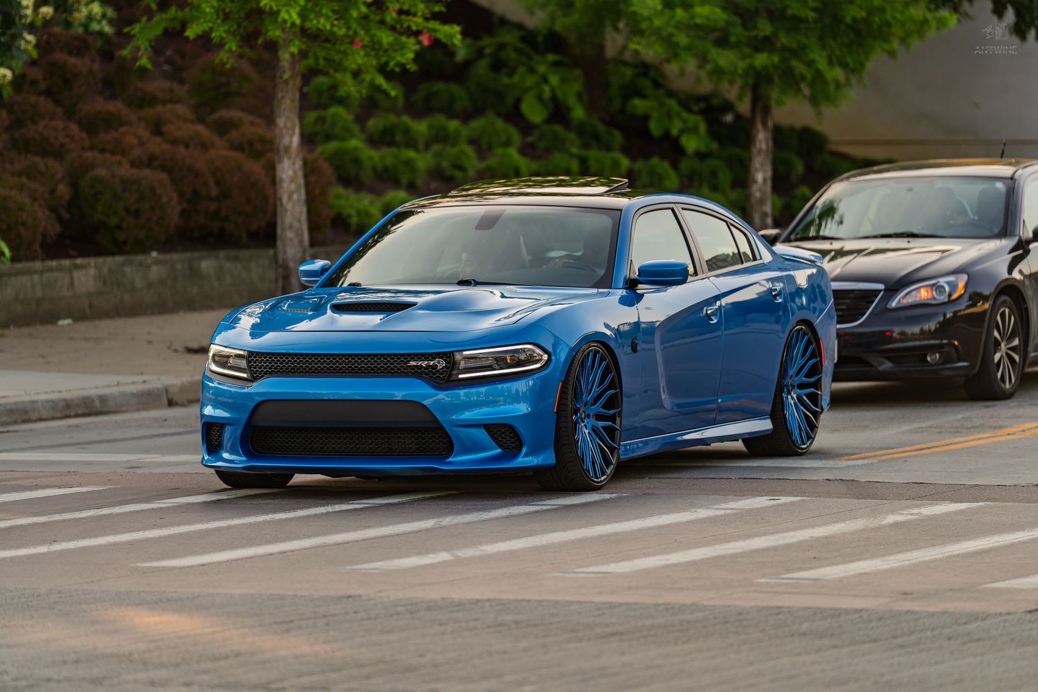 Blue Dodge Charger SRT Hellcat parked on a city street with black cars in the background.