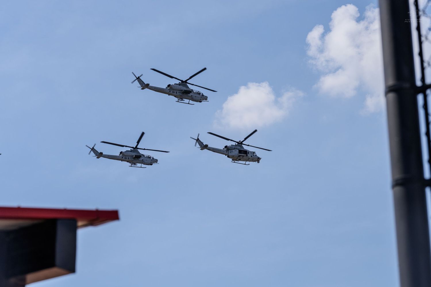 Three military helicopters flying in formation against a partly cloudy blue sky.