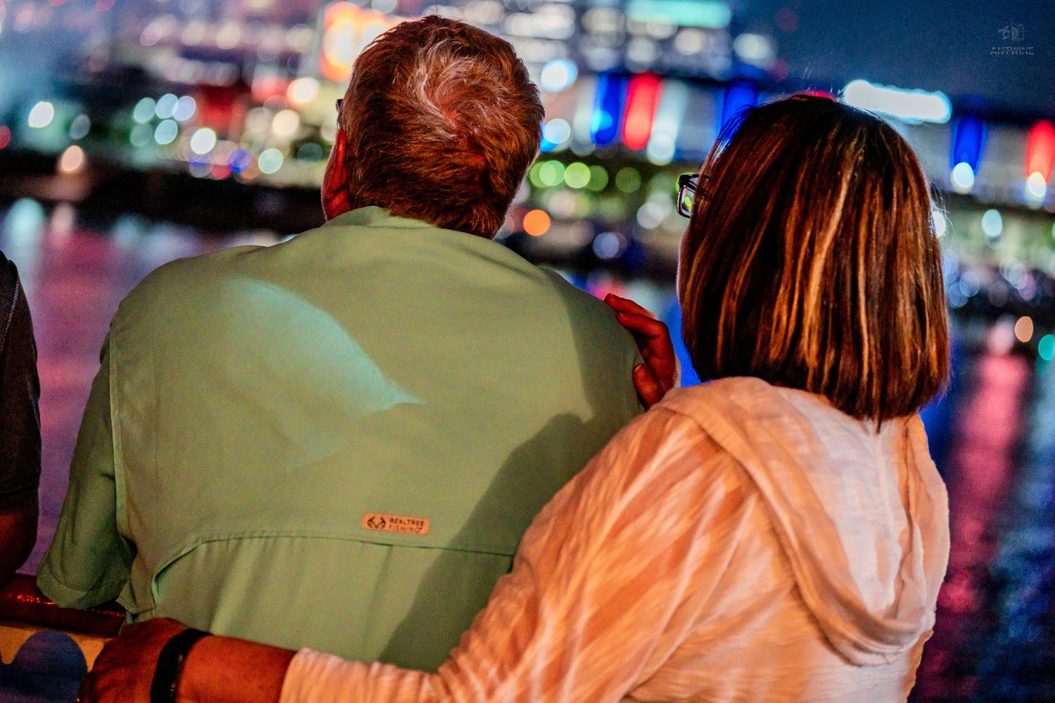 Couple sitting together at night enjoying colorful city lights reflecting on the water behind them.