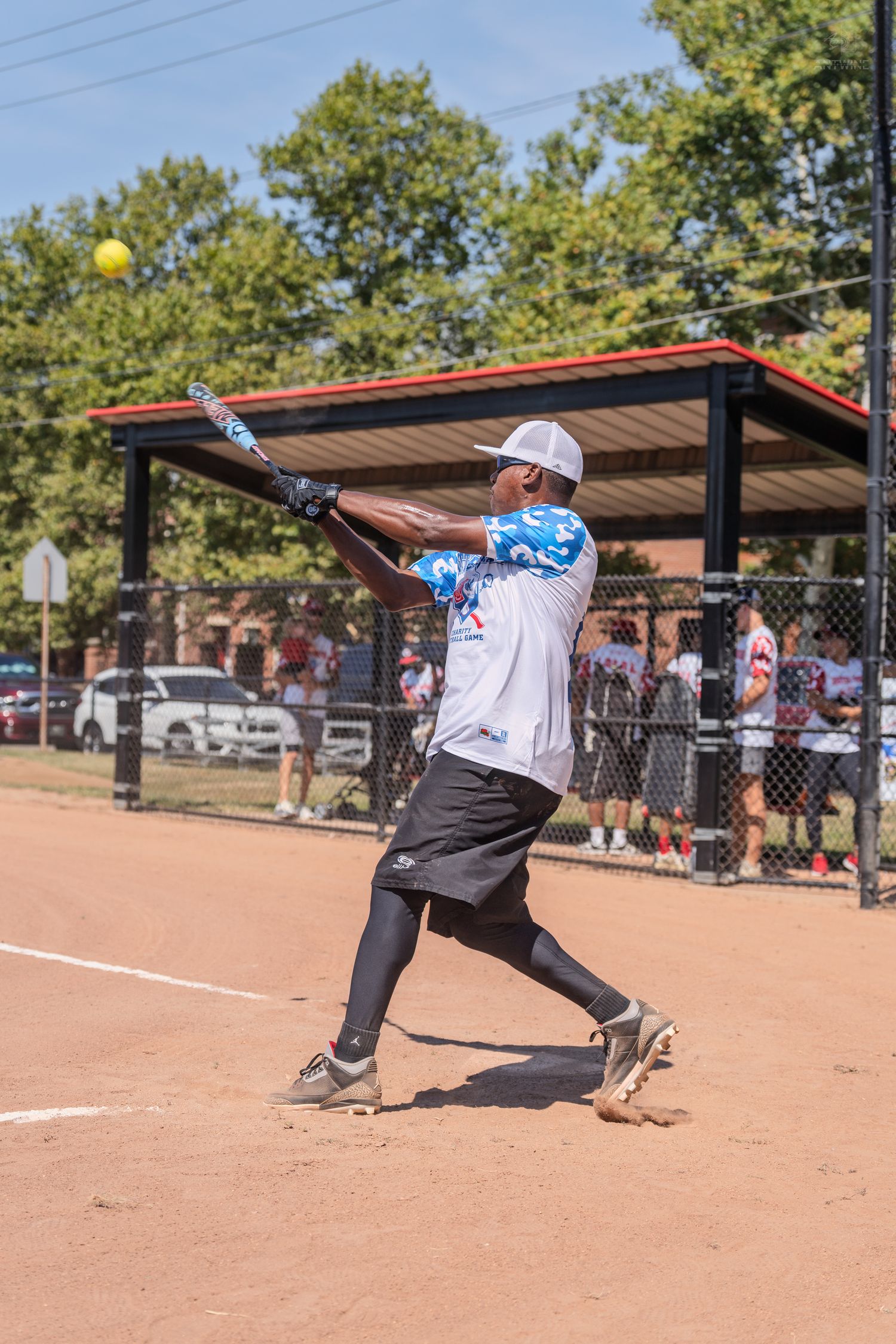 African American softball player swinging bat at yellow ball on dirt field.