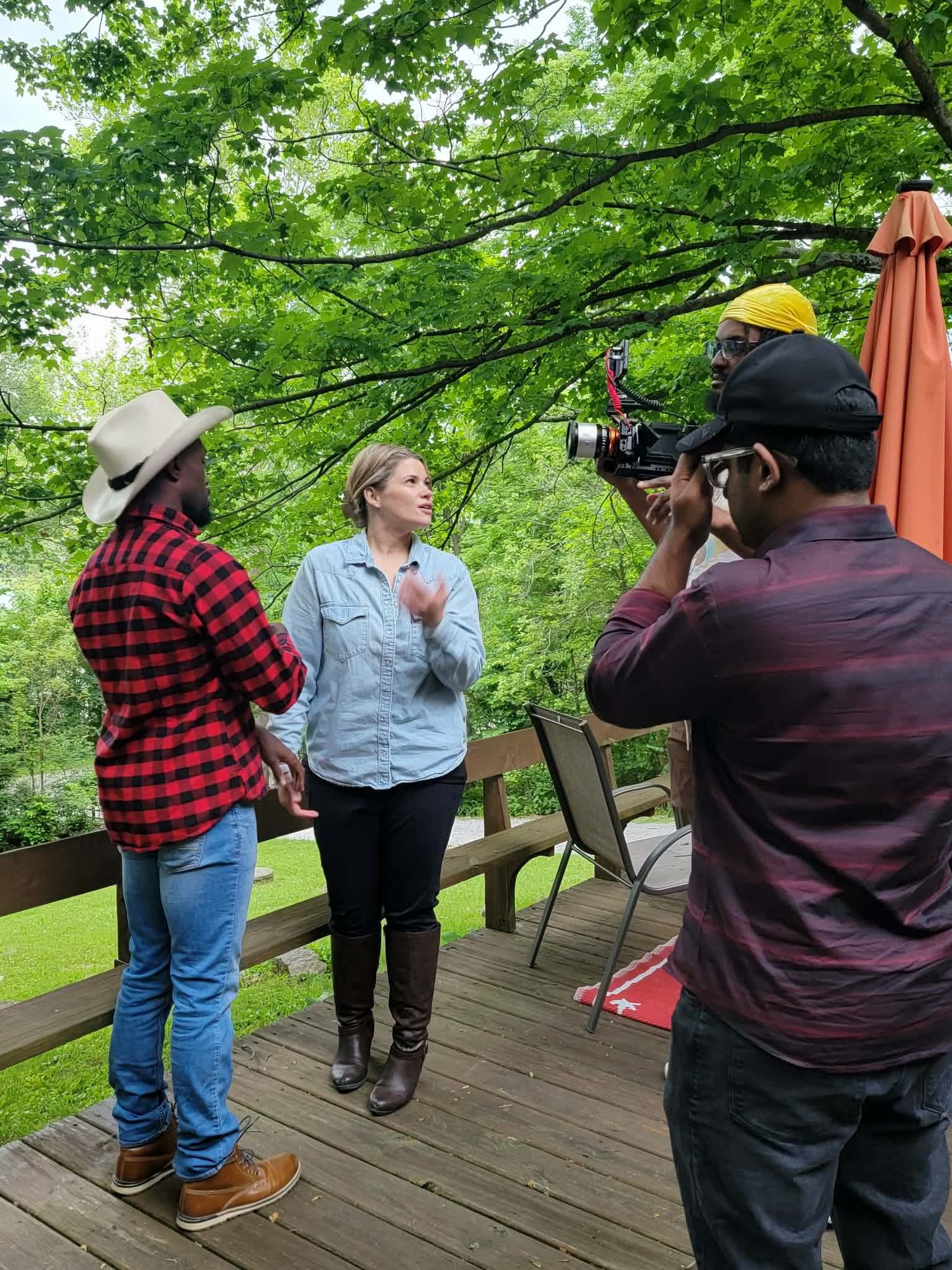 Cameraman filming two actors on wooden deck during outdoor movie production.