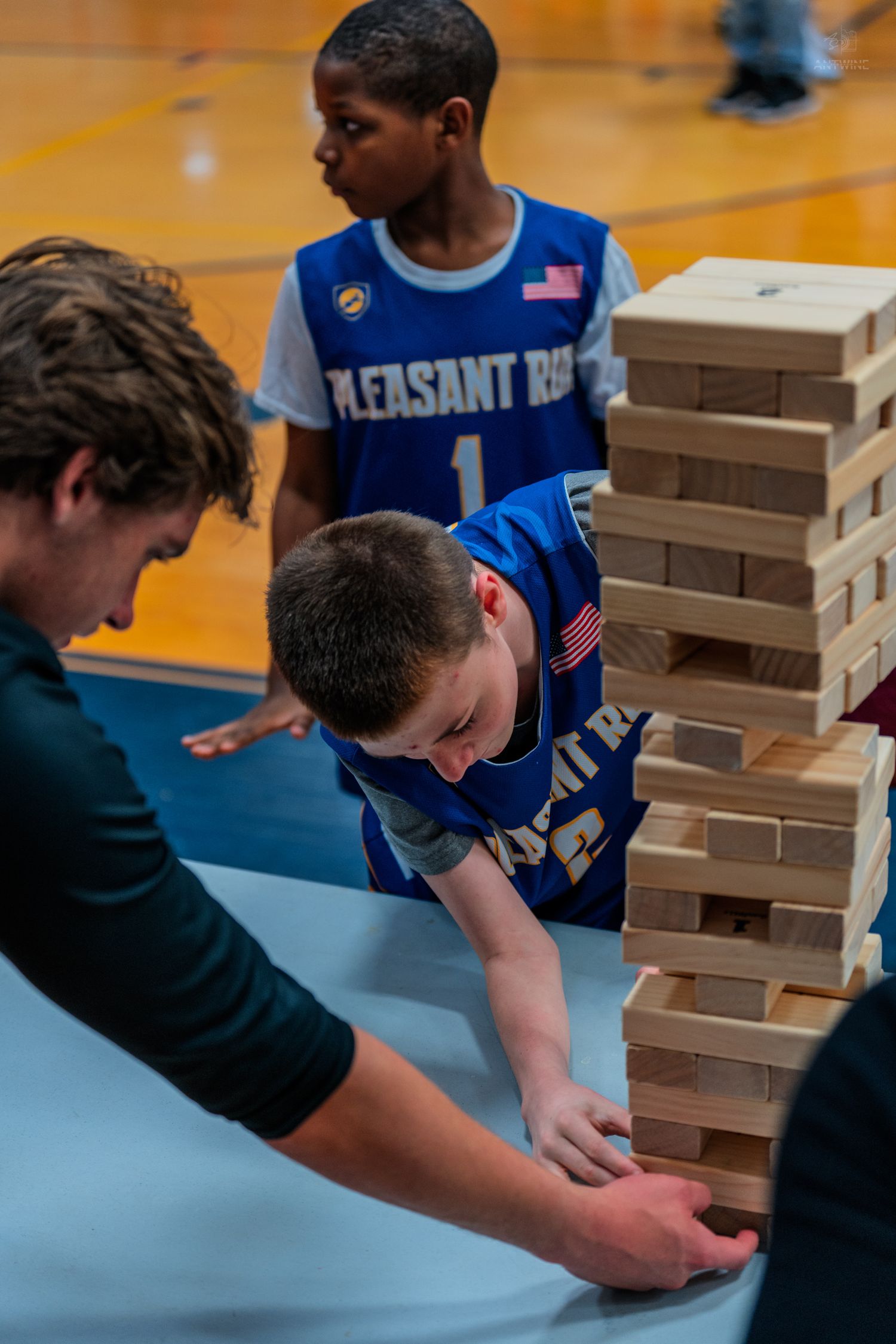 Two boys in Pleasant Run basketball jerseys play Jenga during an indoor recreational event.