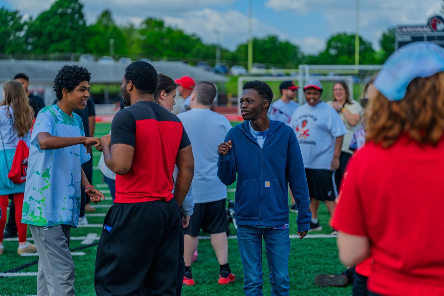 Diverse group of students talking and socializing on a red turf field during an outdoor school gathering.