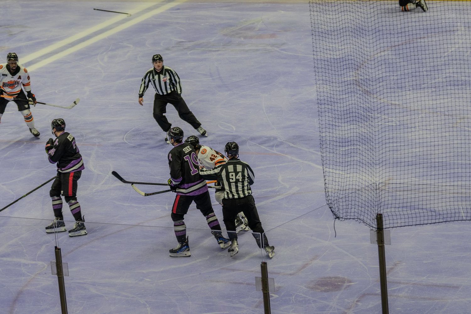 Two ice hockey players face off at center ice as referees oversee the drop during a game.