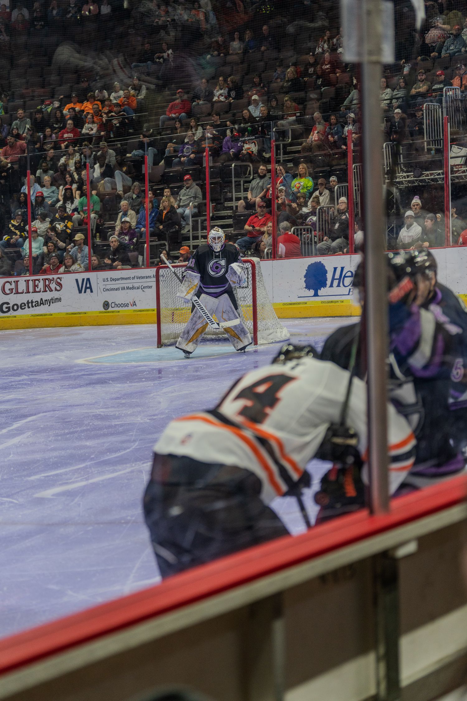 View through the glass of a Fort Wayne Komets player #14 facing the opposing goalie during a hockey game.