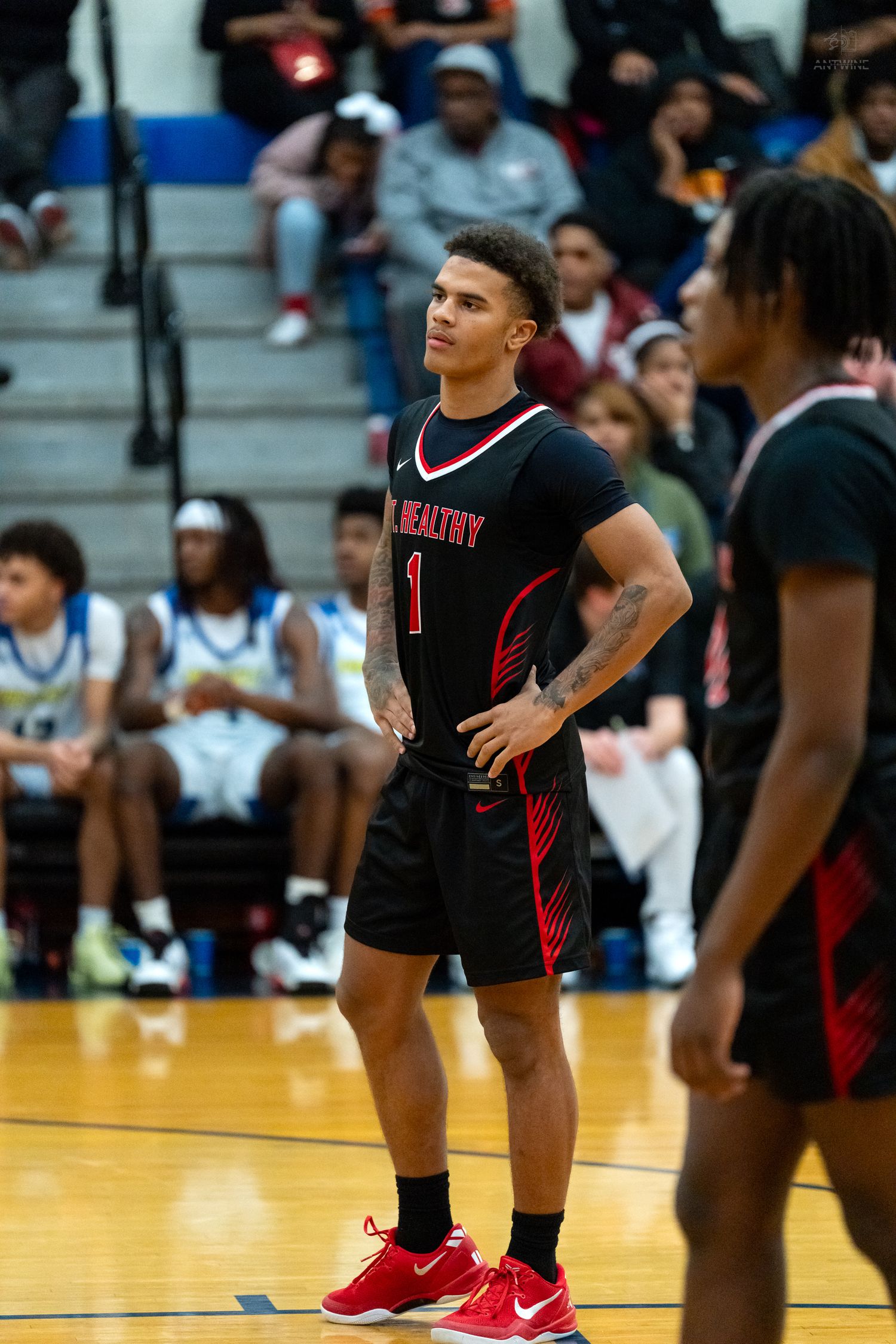 High school basketball player wearing number 1 in black Nike uniform stands confidently on the court.