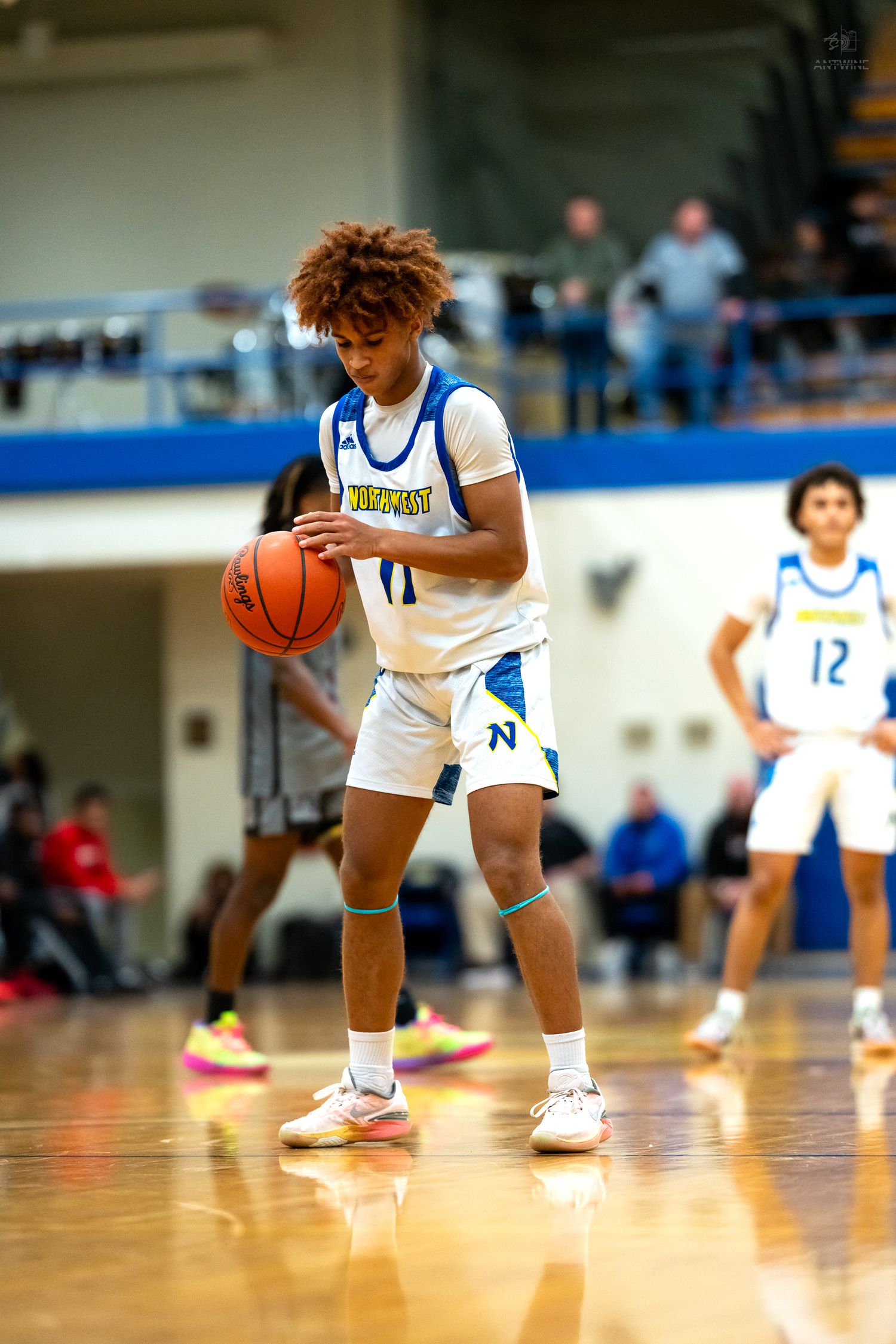 Northwest high school basketball player number 11 handles ball while teammate number 12 stands nearby.