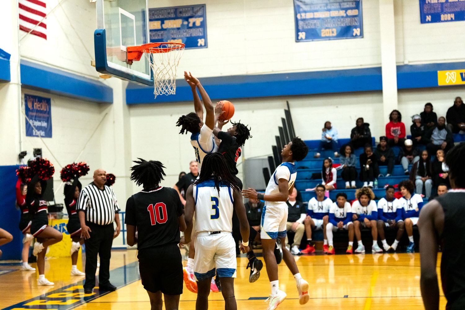 Red jersey player leaps for a layup attempt at the basket during a high school basketball game.
