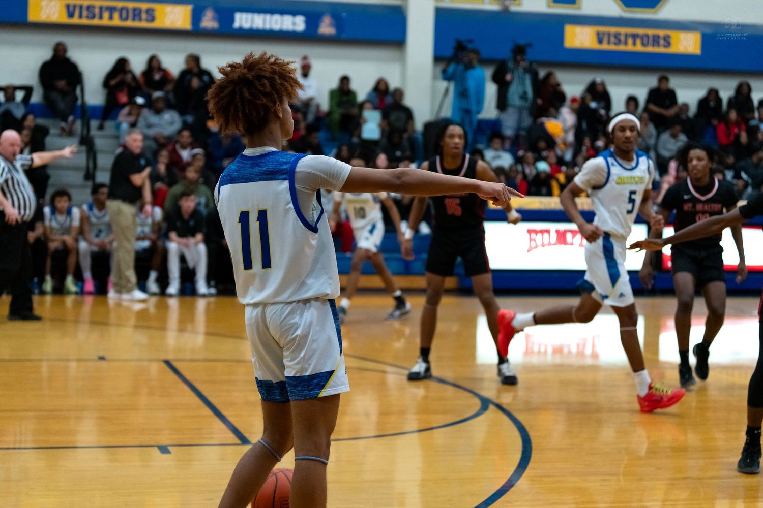 Player in blue number 11 jersey passes the ball during a fast-paced high school basketball game.